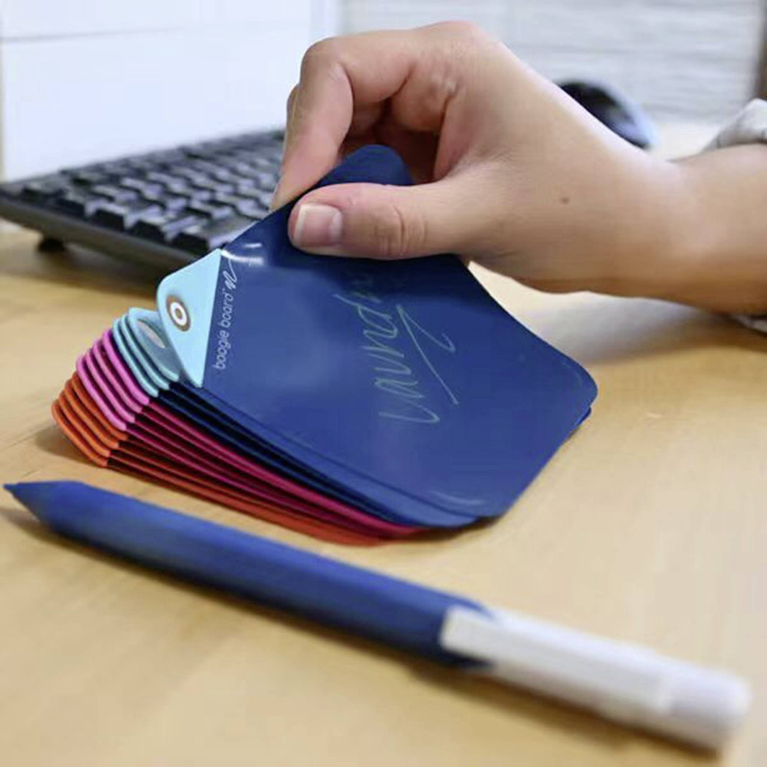 A hand flips through colour swatch fans on a desk, next to a keyboard. Office working environment.