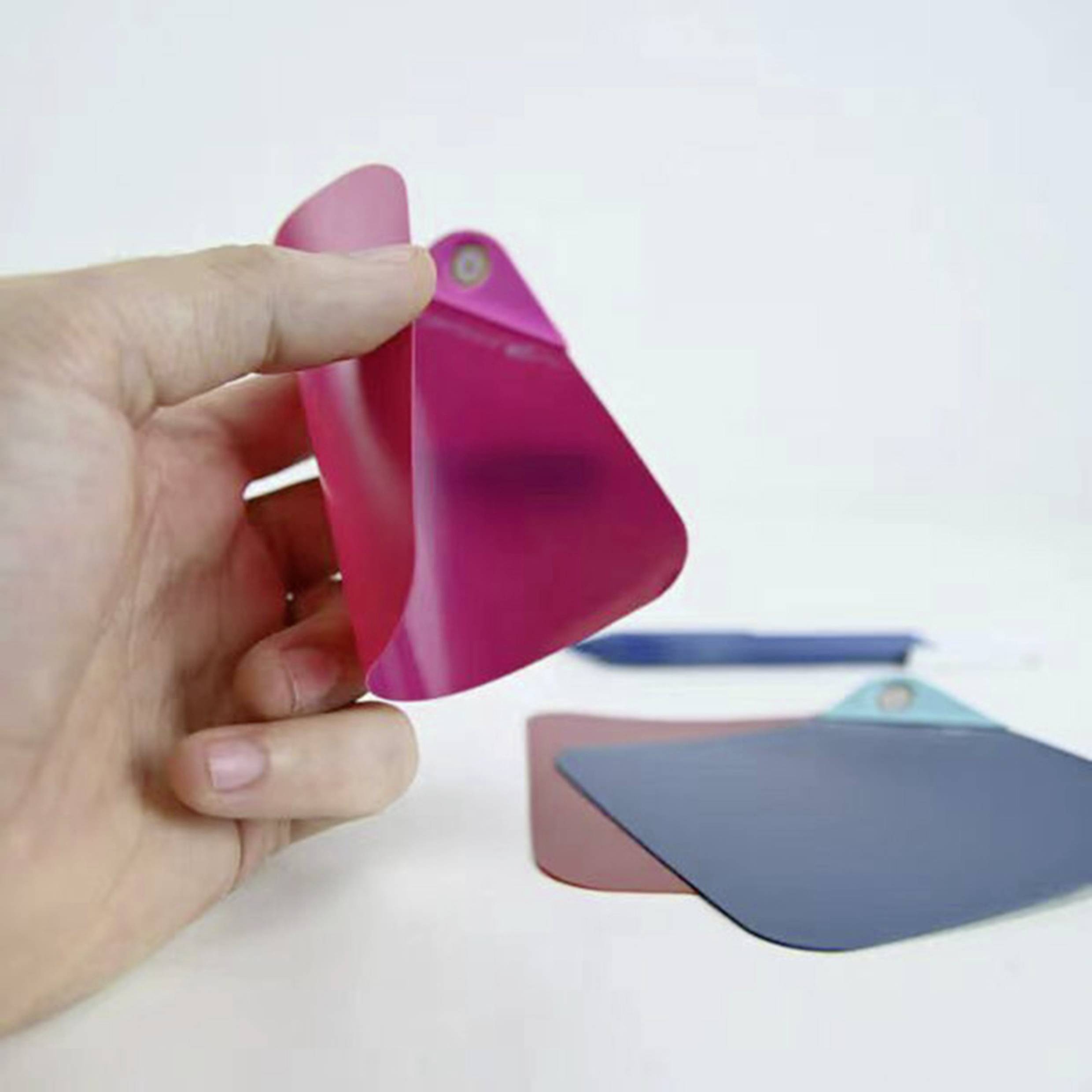 A hand is holding a red colour swatch over a grey and another red card on a table.