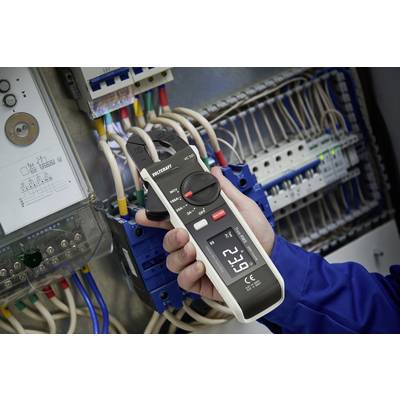 A person is measuring the current flow in an electrical distribution box using a clamp meter. The display shows '52.2 A'.