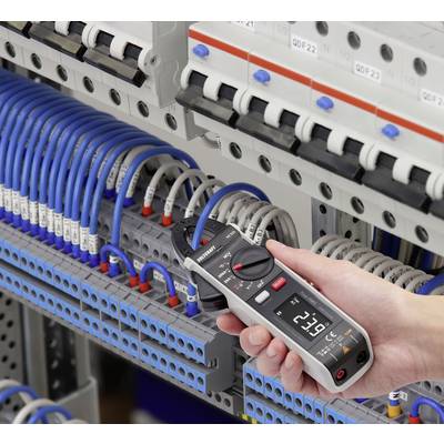 A person is measuring the voltage in an electrical cabinet with a digital multimeter. Cables are connected to various terminals.