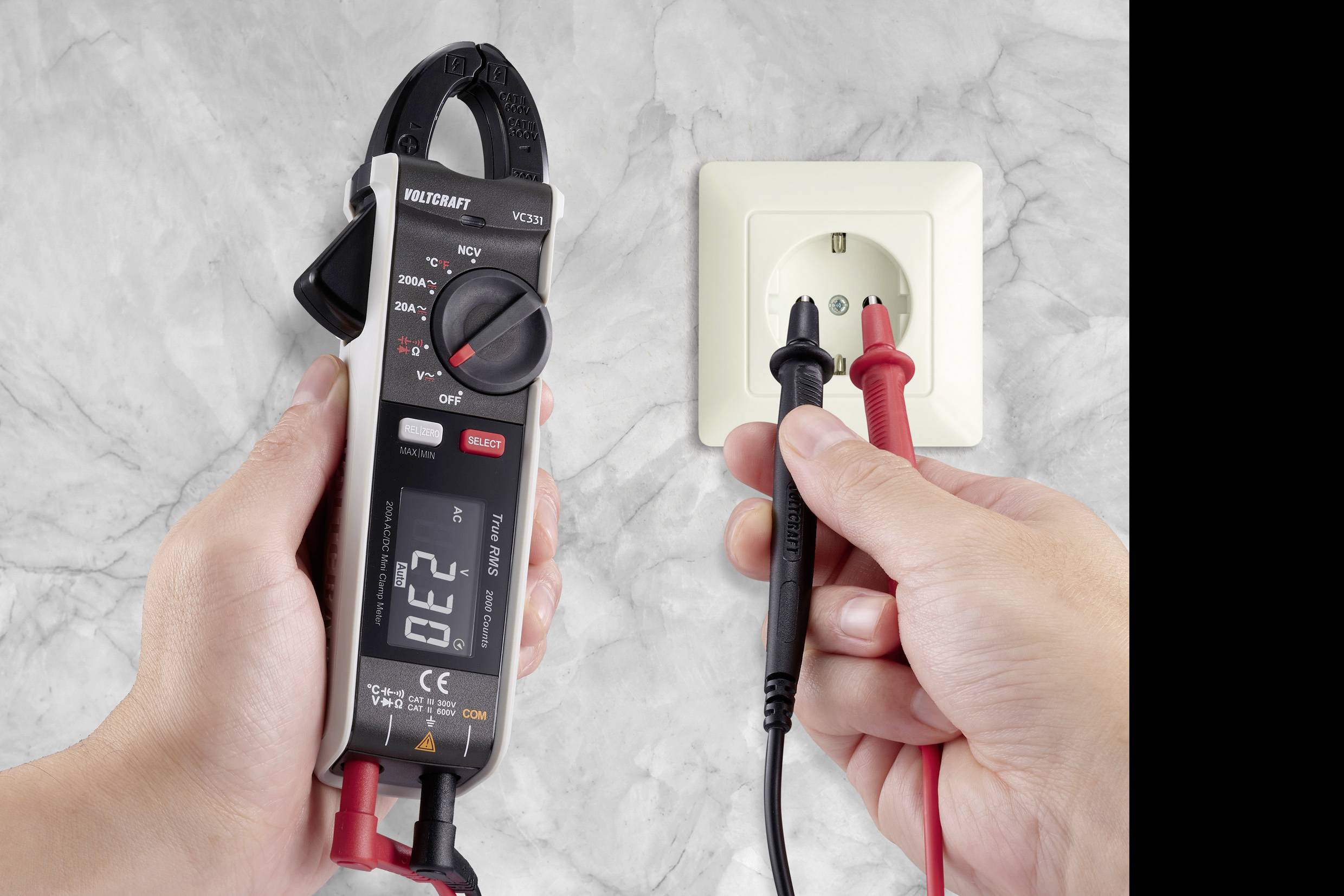 Two hands are testing a power socket with a digital multimeter and test leads. The display shows '0.22', alternating current measurement.