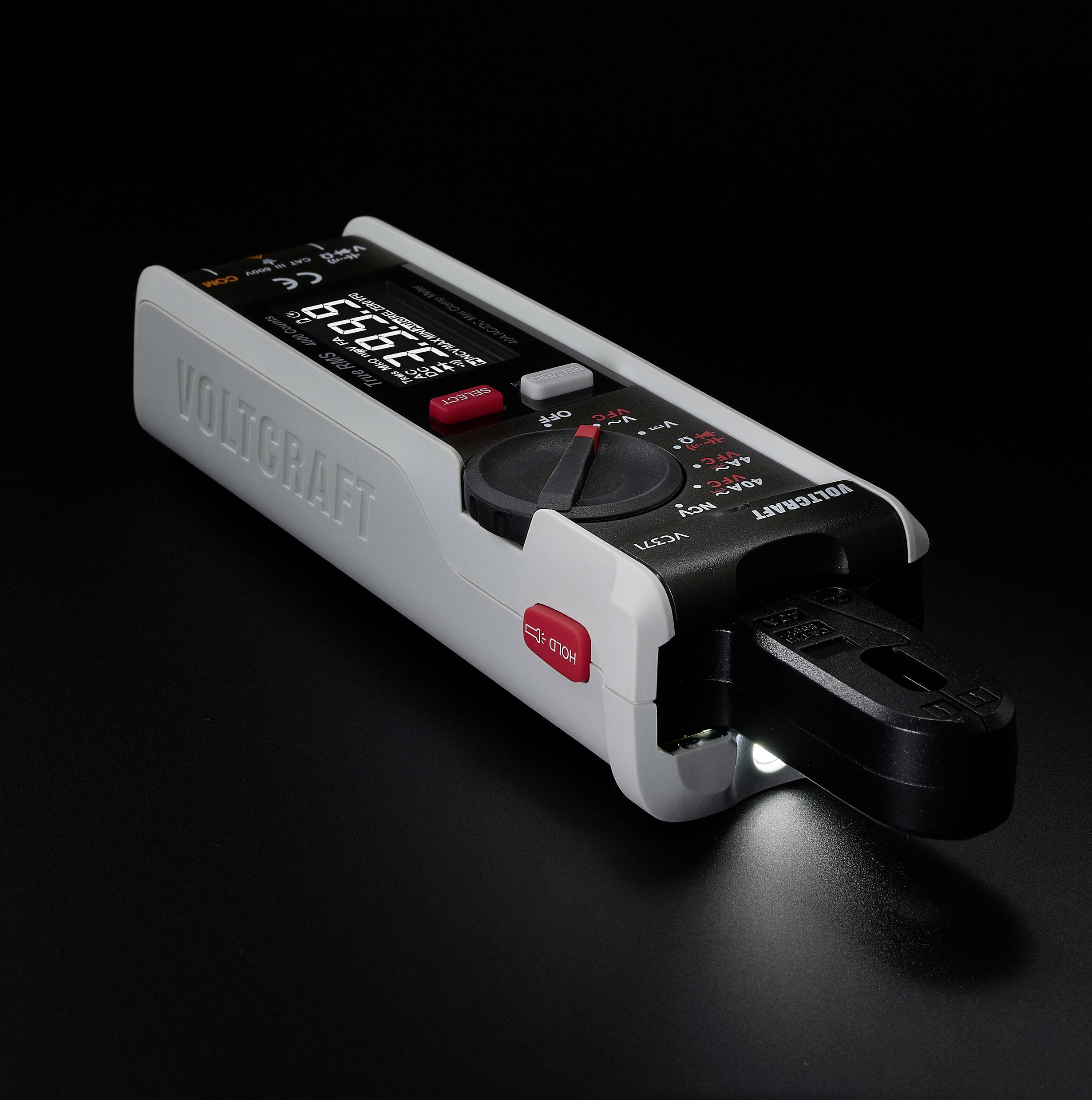 Digital multimeter with illuminated display on a black background. Device shows measurement values and has a red button and rotary dial.