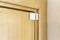 A white magnetic sensor is mounted on a light brown wooden door frame. The sensor is used to monitor the opening and closing of the door.