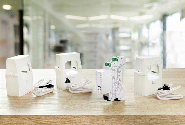Three white current transformers and a module are sitting on a table. The background shows a blurred office. Topic: Electronic devices.