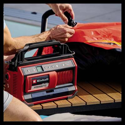 A person is using a red electric pump to inflate an object on a wooden table.