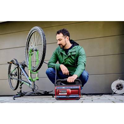 A man in a green anorak is repairing an upturned bicycle using a red electric tool.