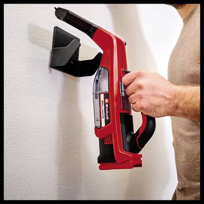 A person is holding a red, cordless handheld vacuum cleaner that is mounted on a wall. The vacuum is secured in a wall bracket.
