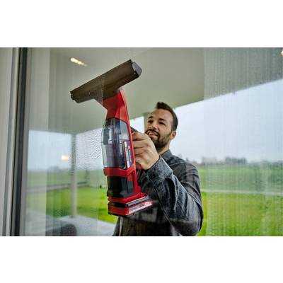 A man thoroughly cleans a large window with a red window squeegee. A green landscape is visible in the background.
