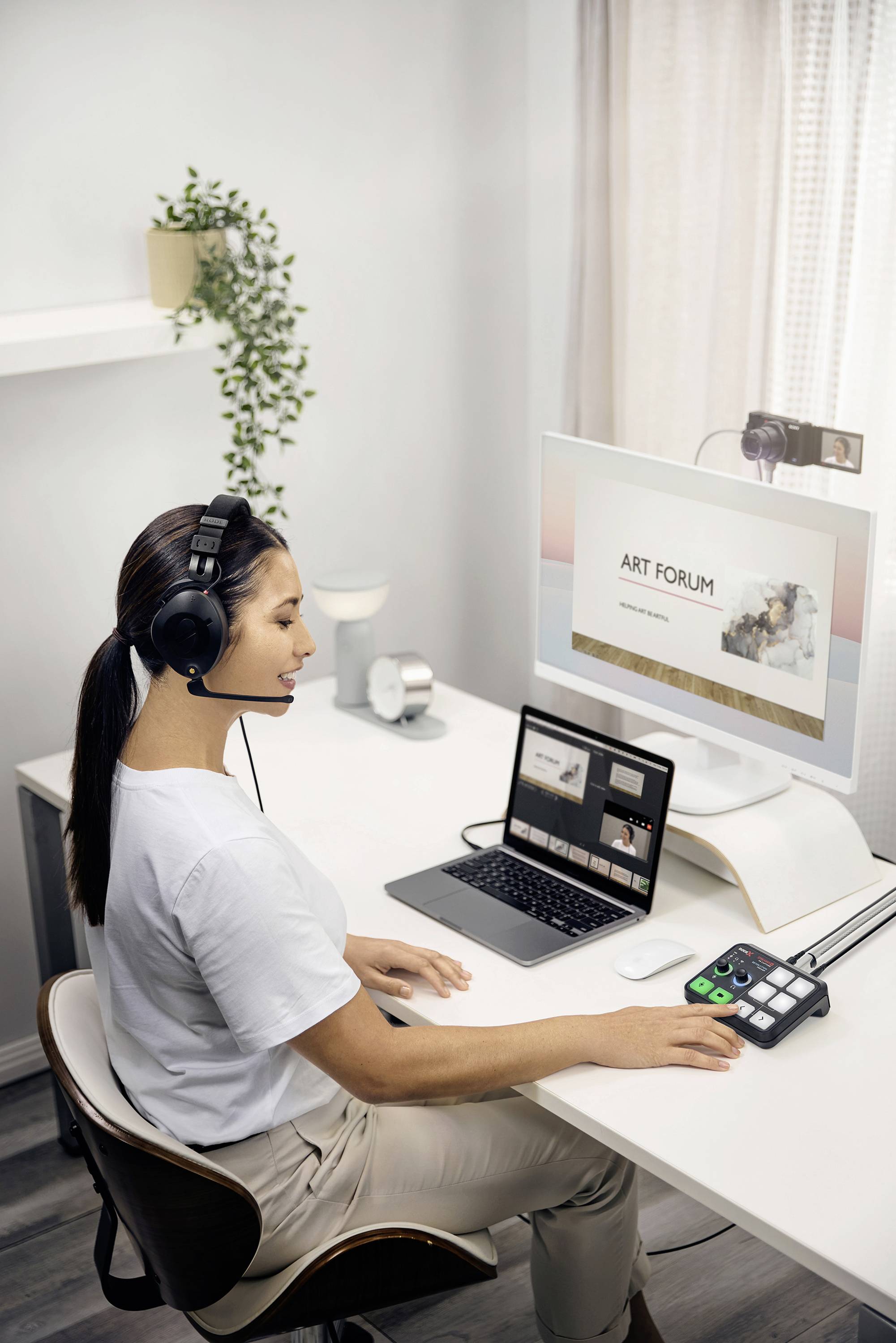 A woman is sitting at a desk with headphones and a microphone, in front of a laptop and a monitor displaying 'Art Forum'.