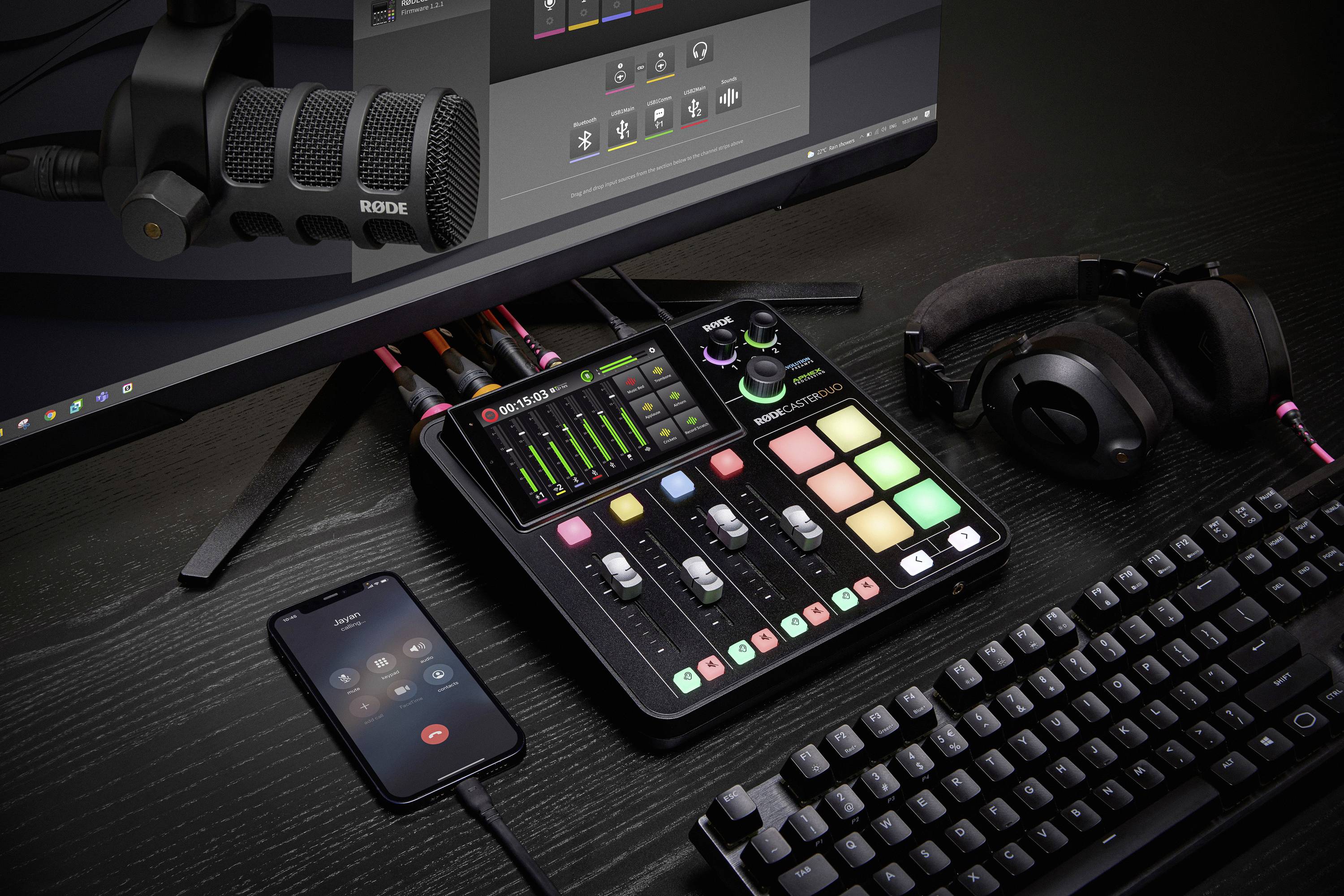 'Podcast setup with microphone, mixing desk, headphones and computer screen. Mixing desk displays LED levels and colourful buttons for control.'