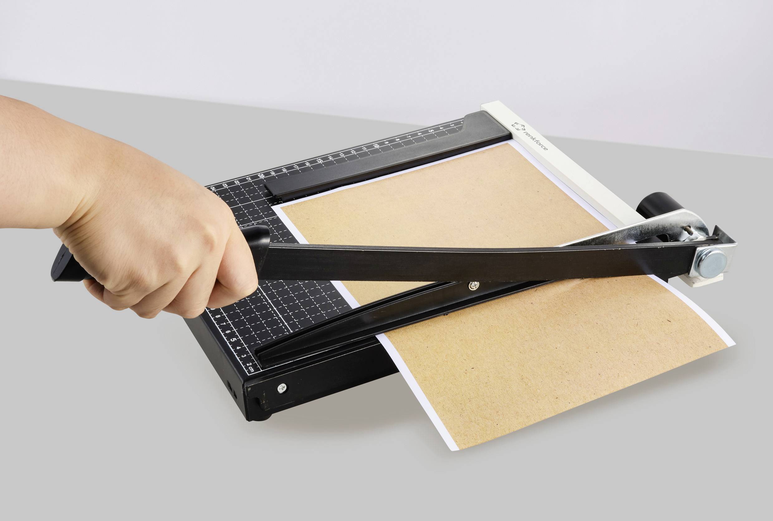 A person is cutting a sheet of paper with a lever cutter. The paper has two different coloured surfaces, brown and white.