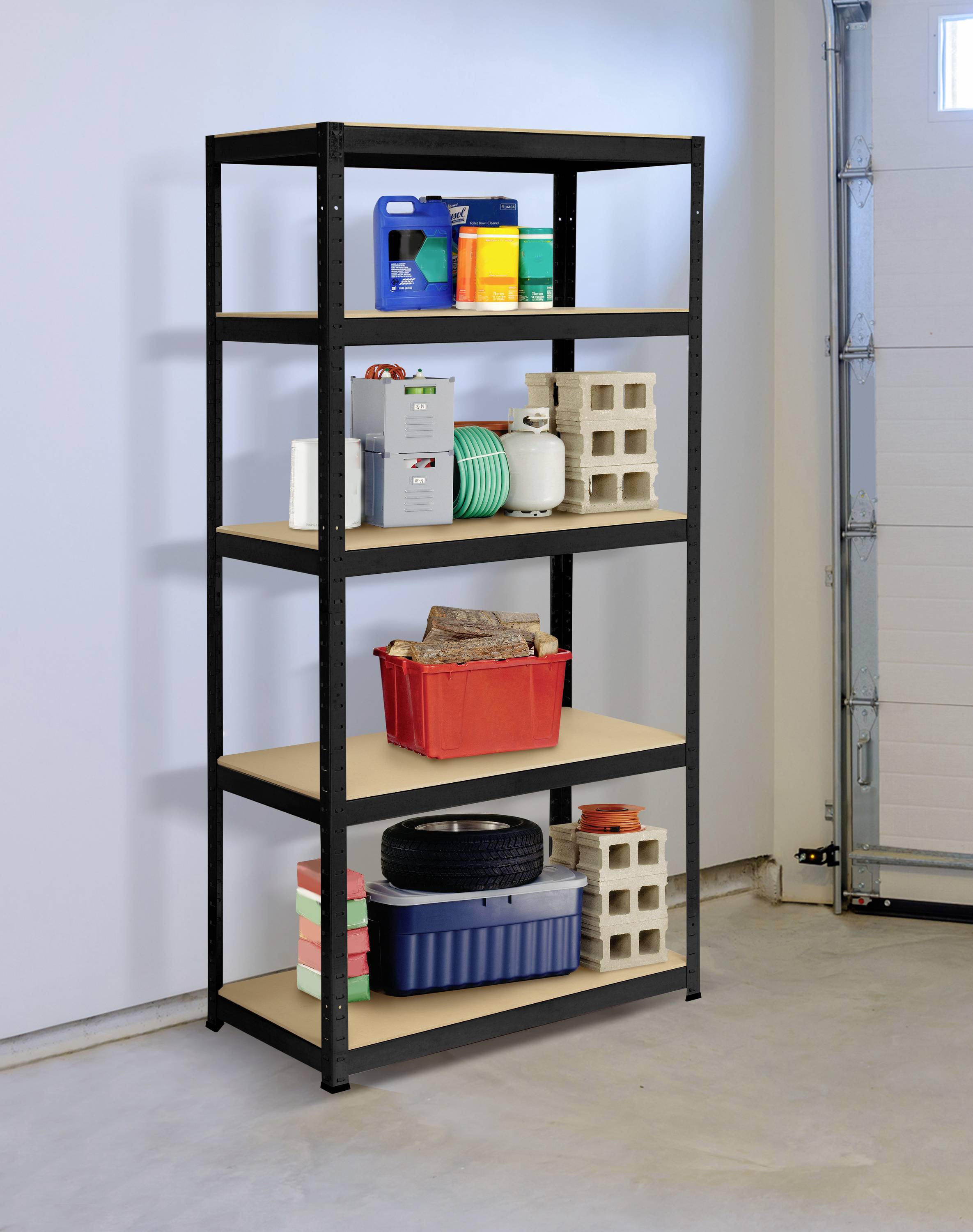 A metal shelving unit with five shelves stands in a garage, loaded with paint tins, a cable, a toolbox, tyres, and bricks.