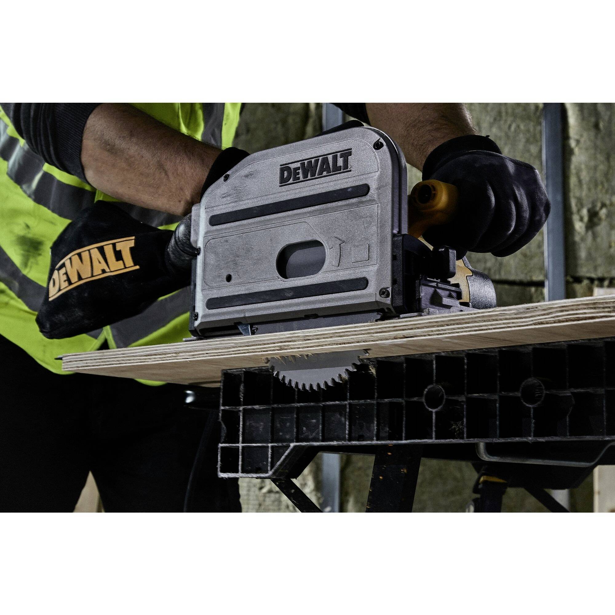 A person in work attire is using a DeWalt circular saw to cut a wooden board. The saw is resting on a workbench.