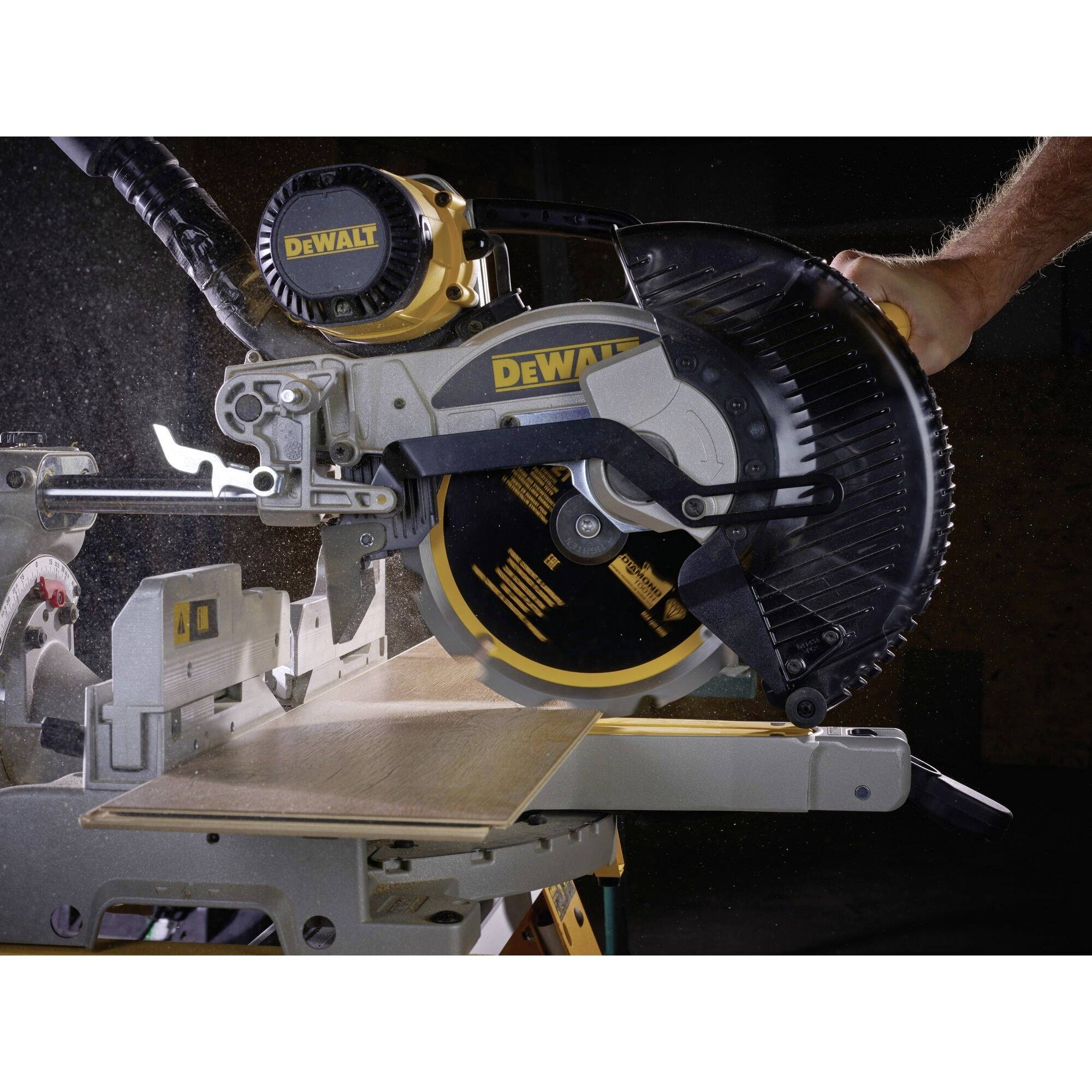 A hand is operating a DeWalt table saw. The saw is cutting a wooden board in a workshop environment.