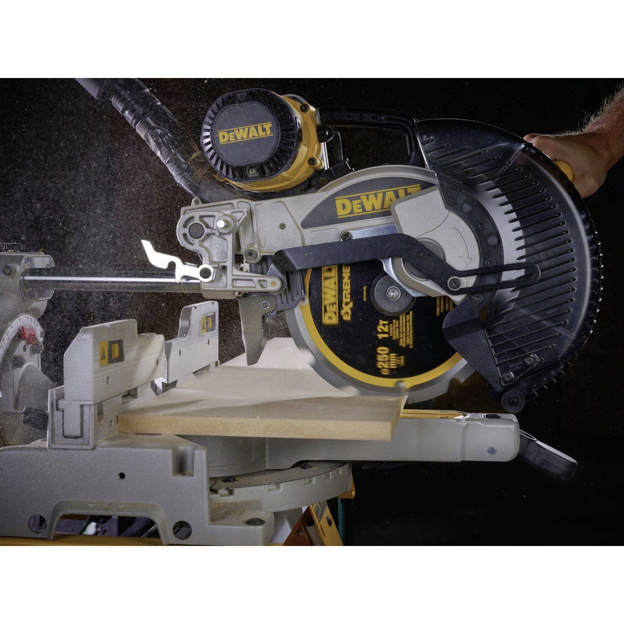 An electric mitre saw cuts a wooden board precisely. Dust particles are visible in the air.