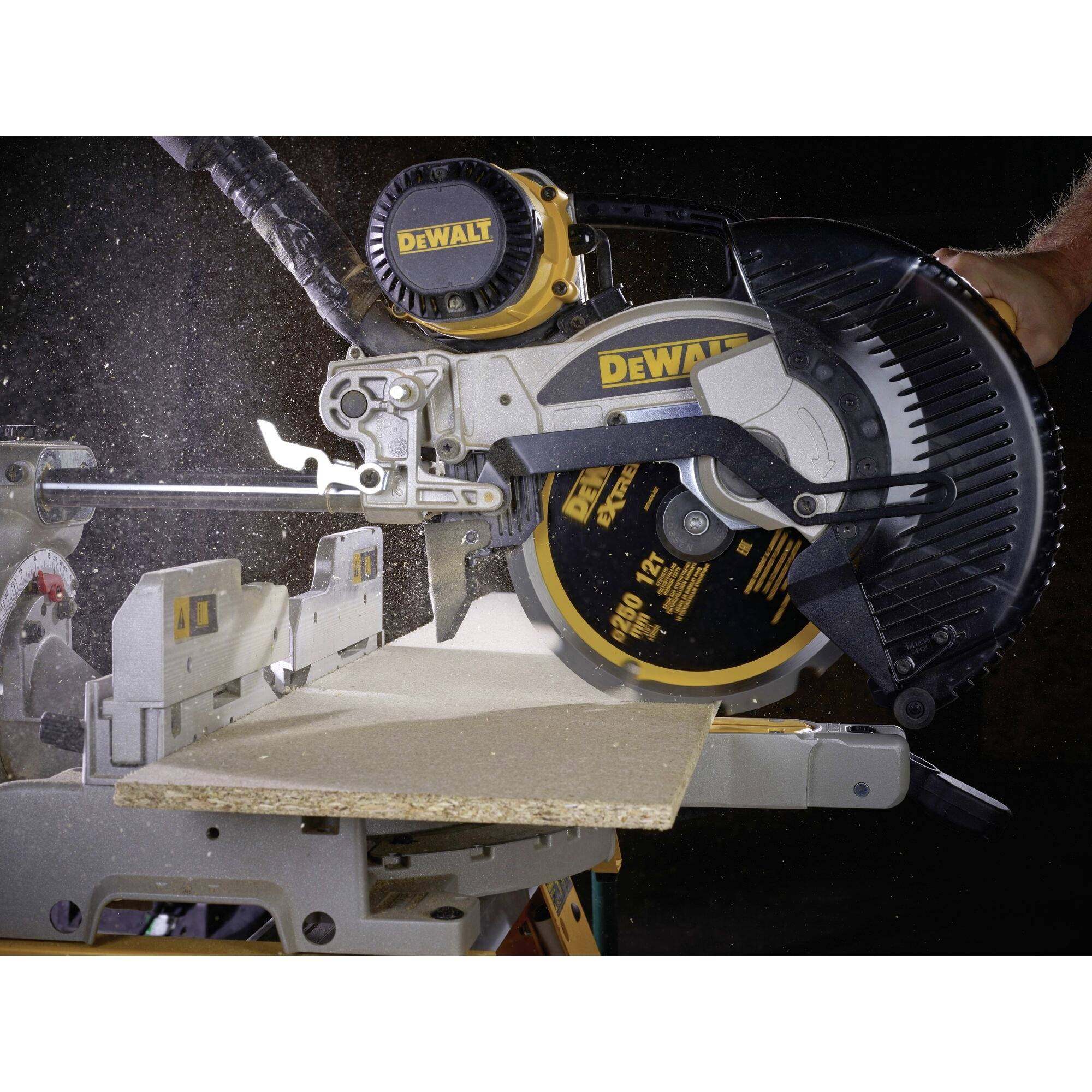 An electric mitre saw cuts a wooden board. Dust particles fly through the air. The scene shows precision work.