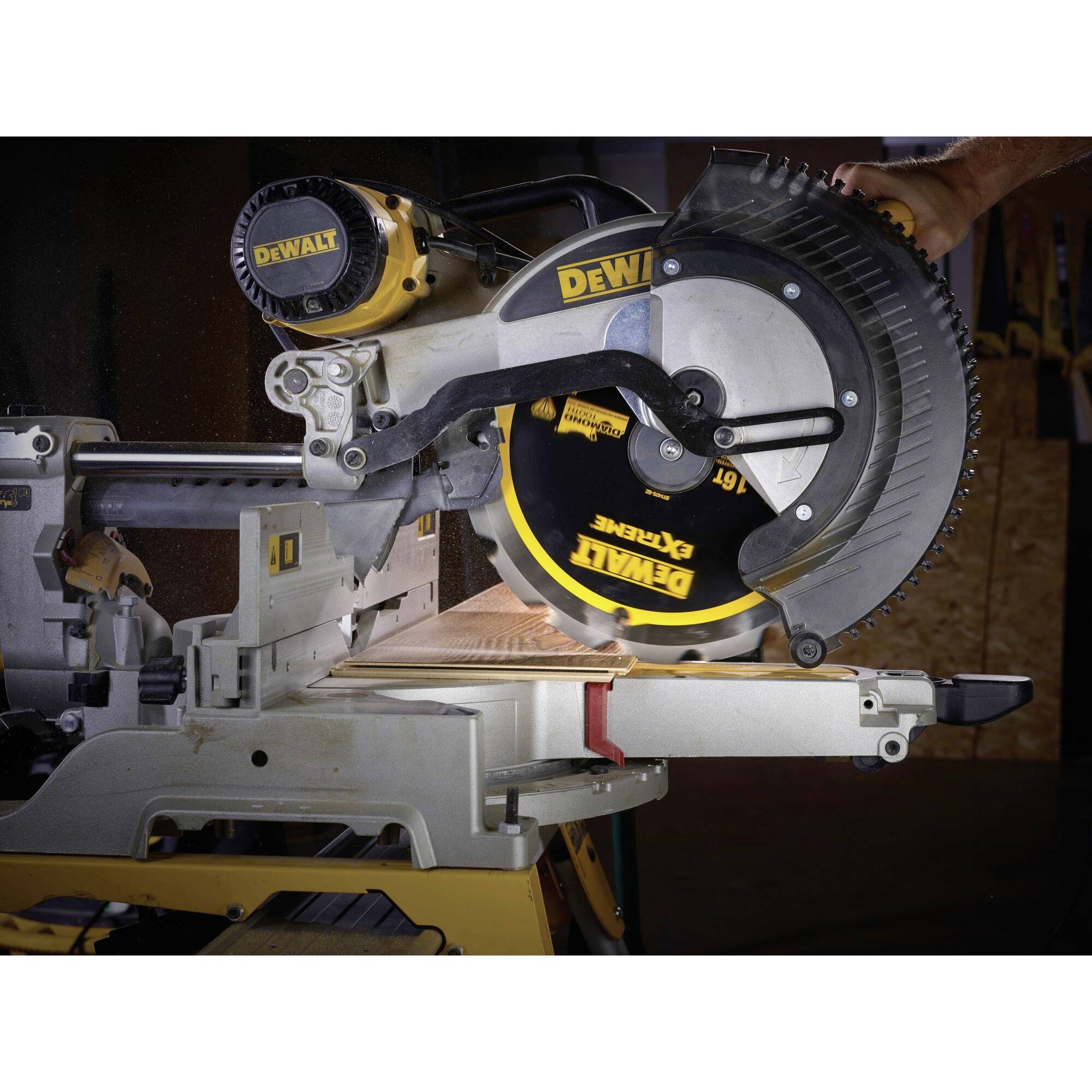 The image shows a stationary DeWalt chop saw cutting a wooden board. A hand is guiding the saw.