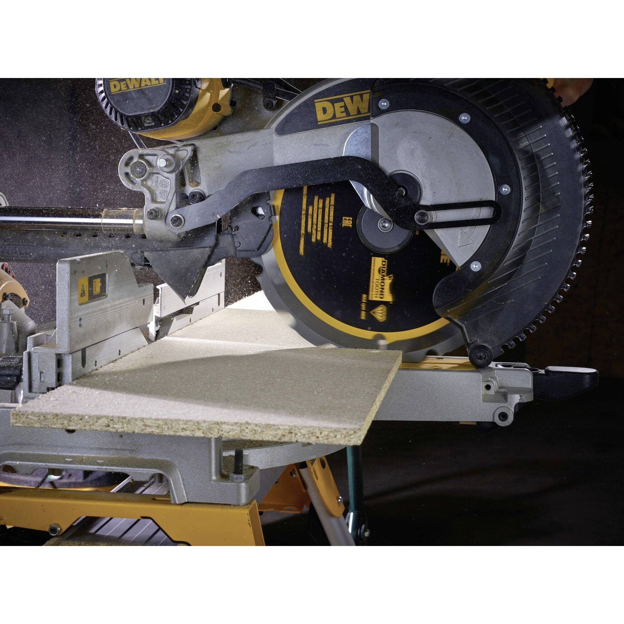 Mitre saw cutting a wooden board in a workshop. The saw is yellow and black, with the surroundings dimly lit.