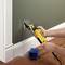 A person precisely cuts a rectangular hole in a green wall with a yellow electric tool. Dust falls to the floor.