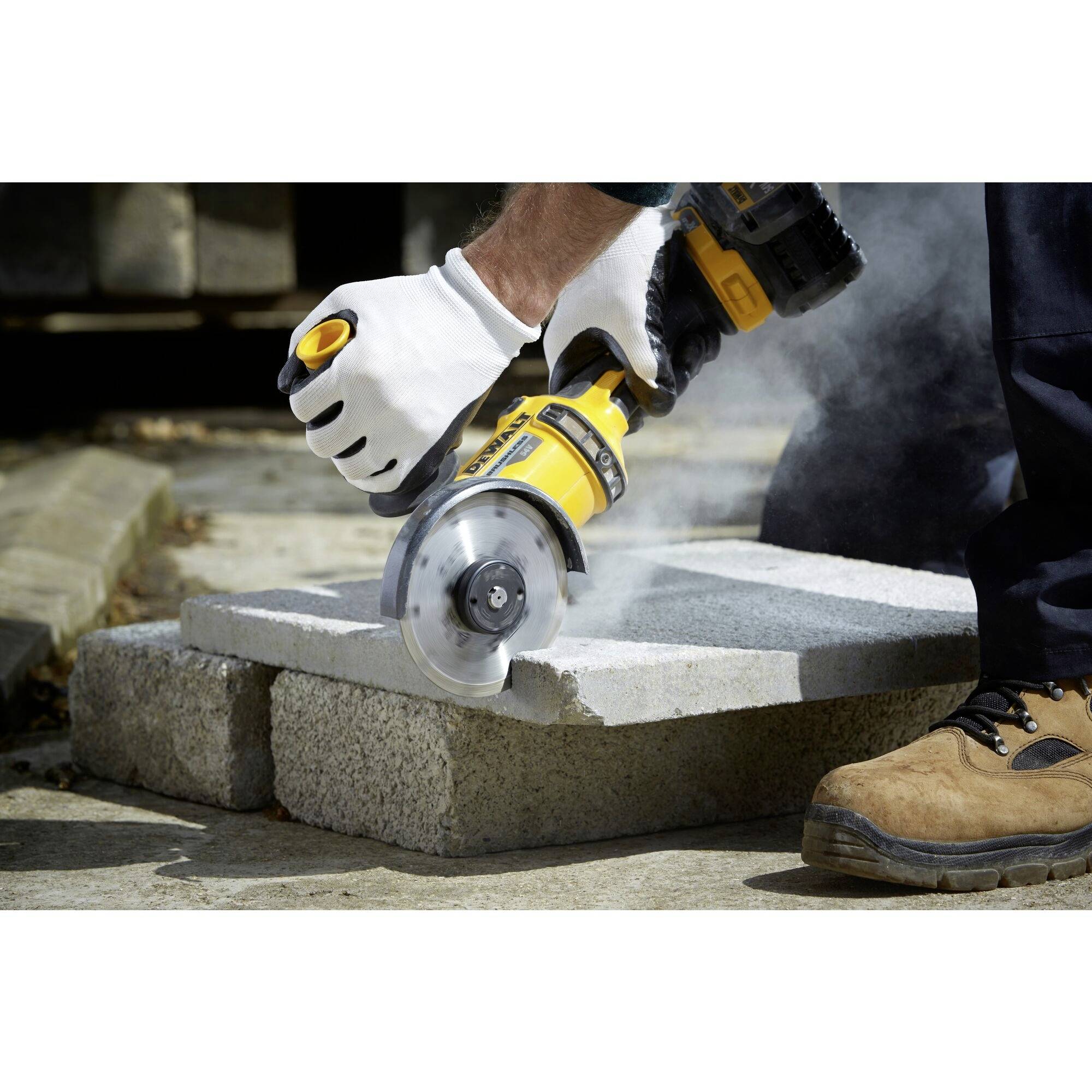 A person is cutting concrete slabs with an electric angle grinder. Dust rises as the blade cuts through the surface.