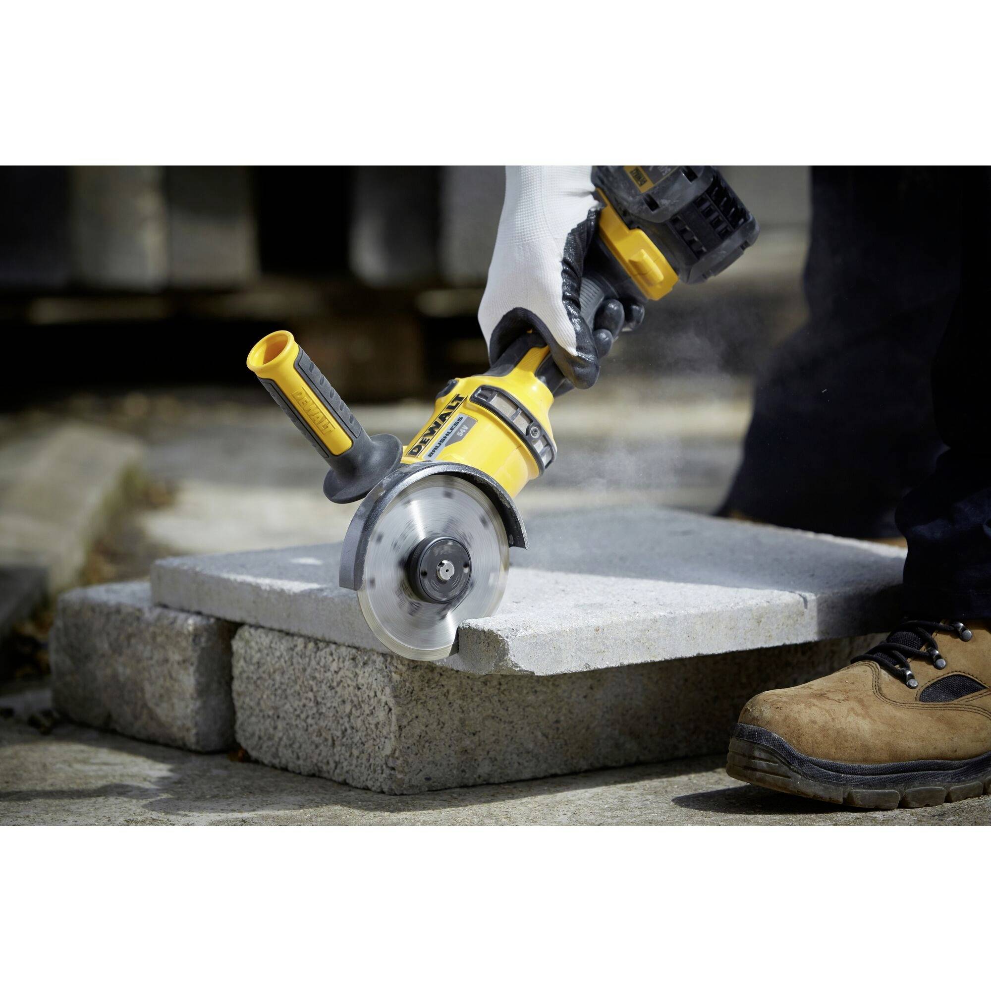 A person is cutting a stone block with a yellow, electric angle grinder. Safety shoes are visible.