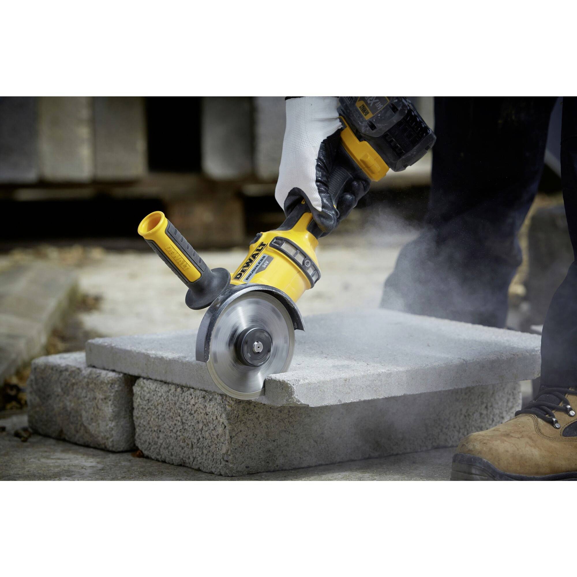 A person is cutting concrete blocks with a yellow angle grinder. Dust is rising.