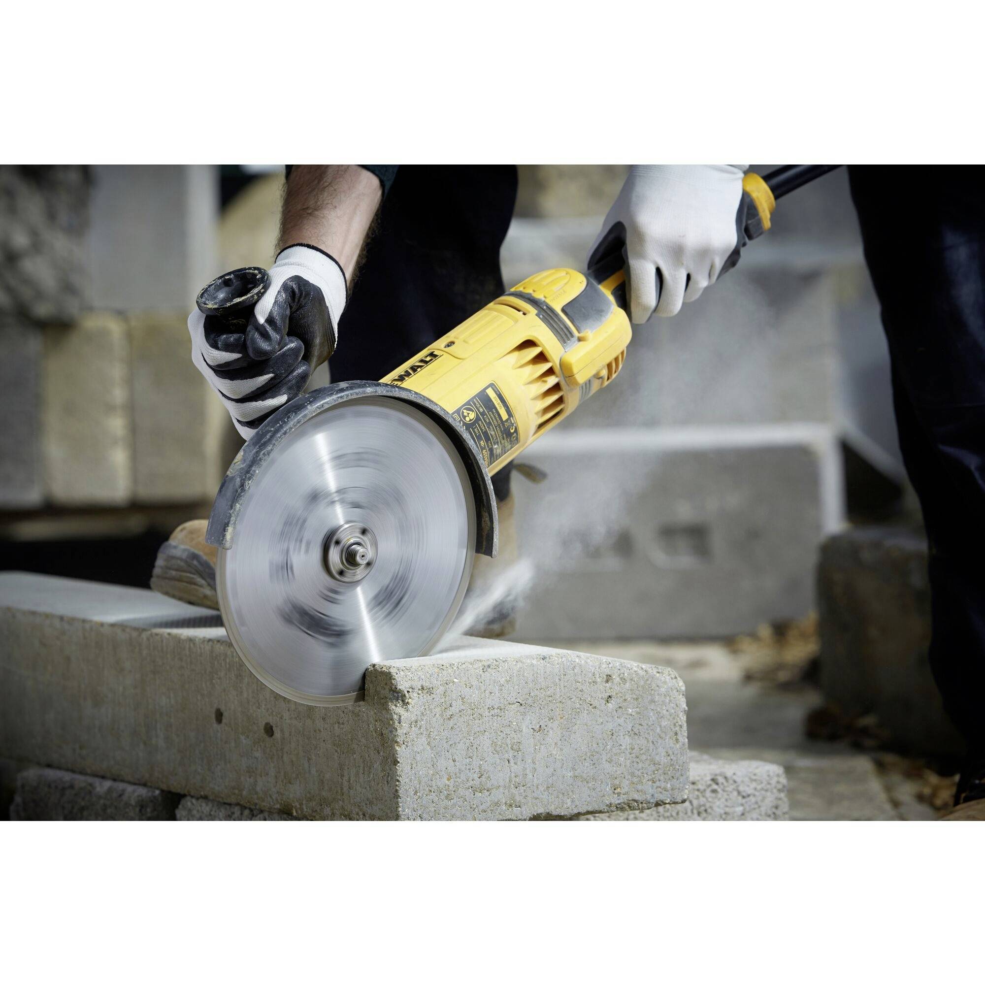 A worker is cutting a concrete block with an electric saw. Protective clothing and gloves are visible.