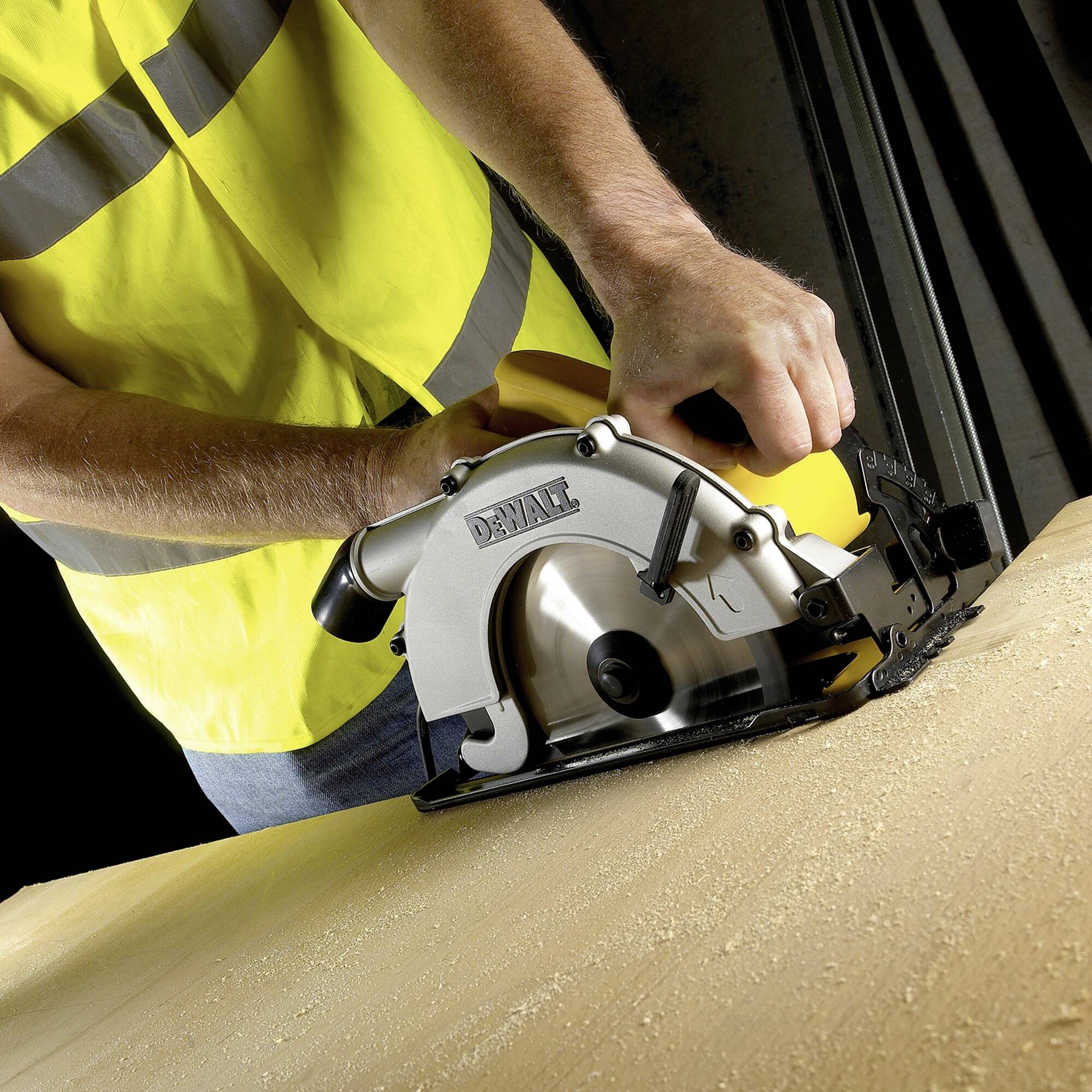 A person in yellow protective clothing is cutting wood with a handheld circular saw. Wood shavings are flying during the cutting process.