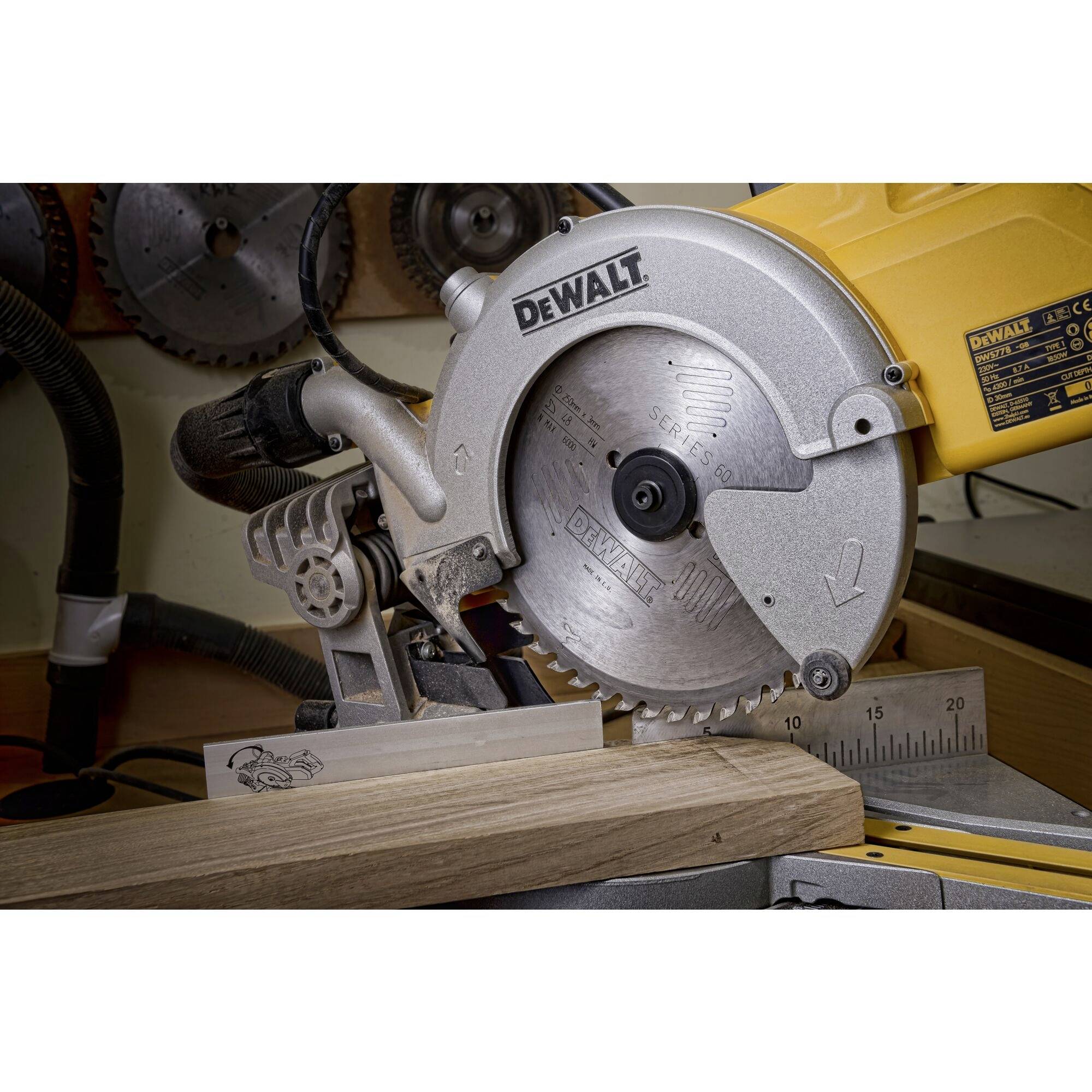 An electric mitre saw is cutting a wooden board in a workshop. The saw has a silver saw blade and a yellow body.