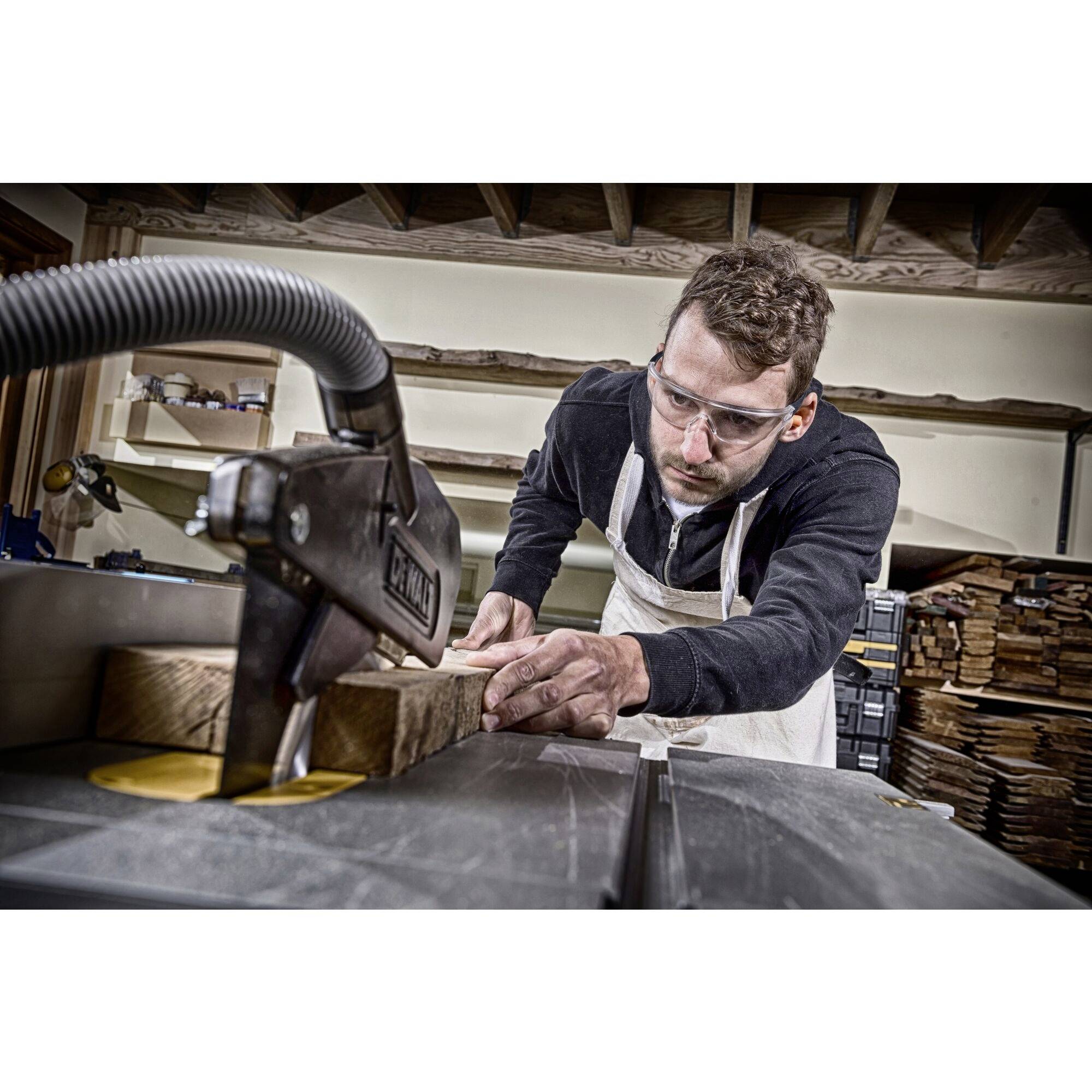 A man is wearing safety glasses and an apron while machining wood with a machine in a workshop.