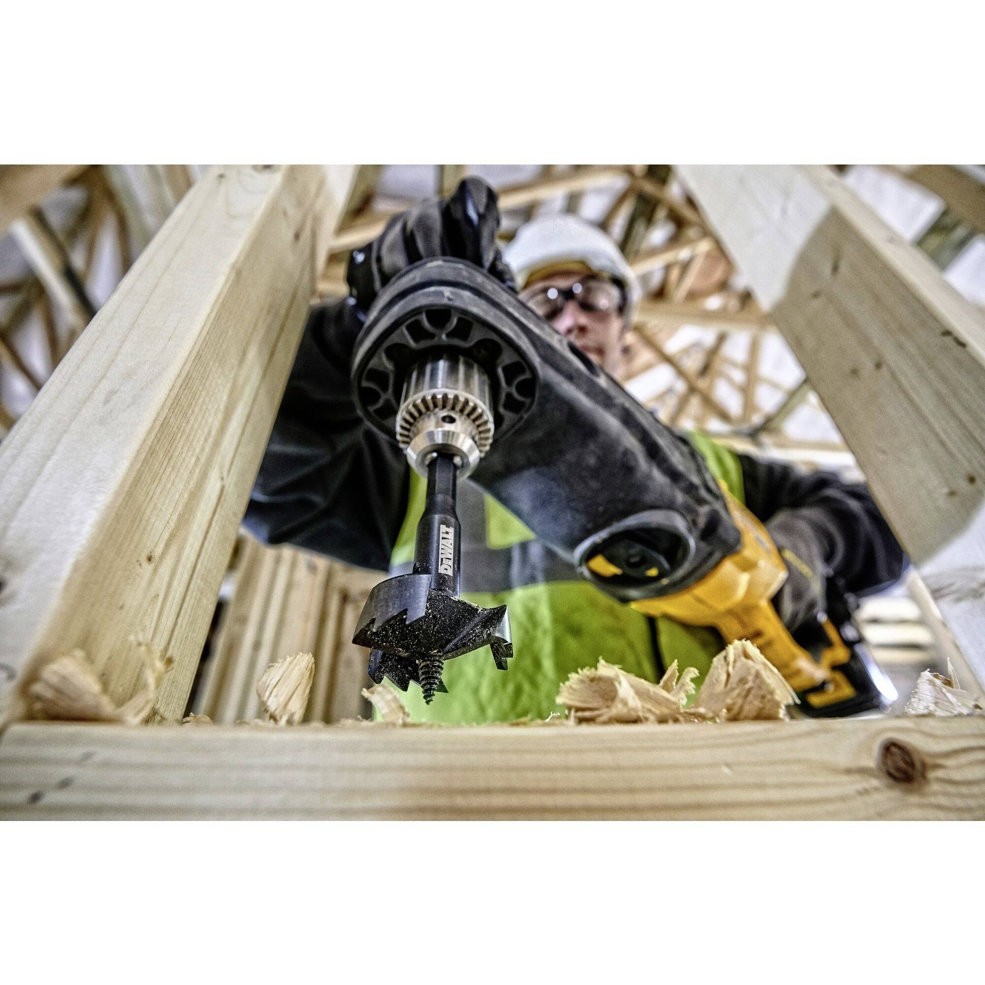 A construction worker is drilling wood with a high-powered machine in a building, surrounded by wooden frames and scaffolding.