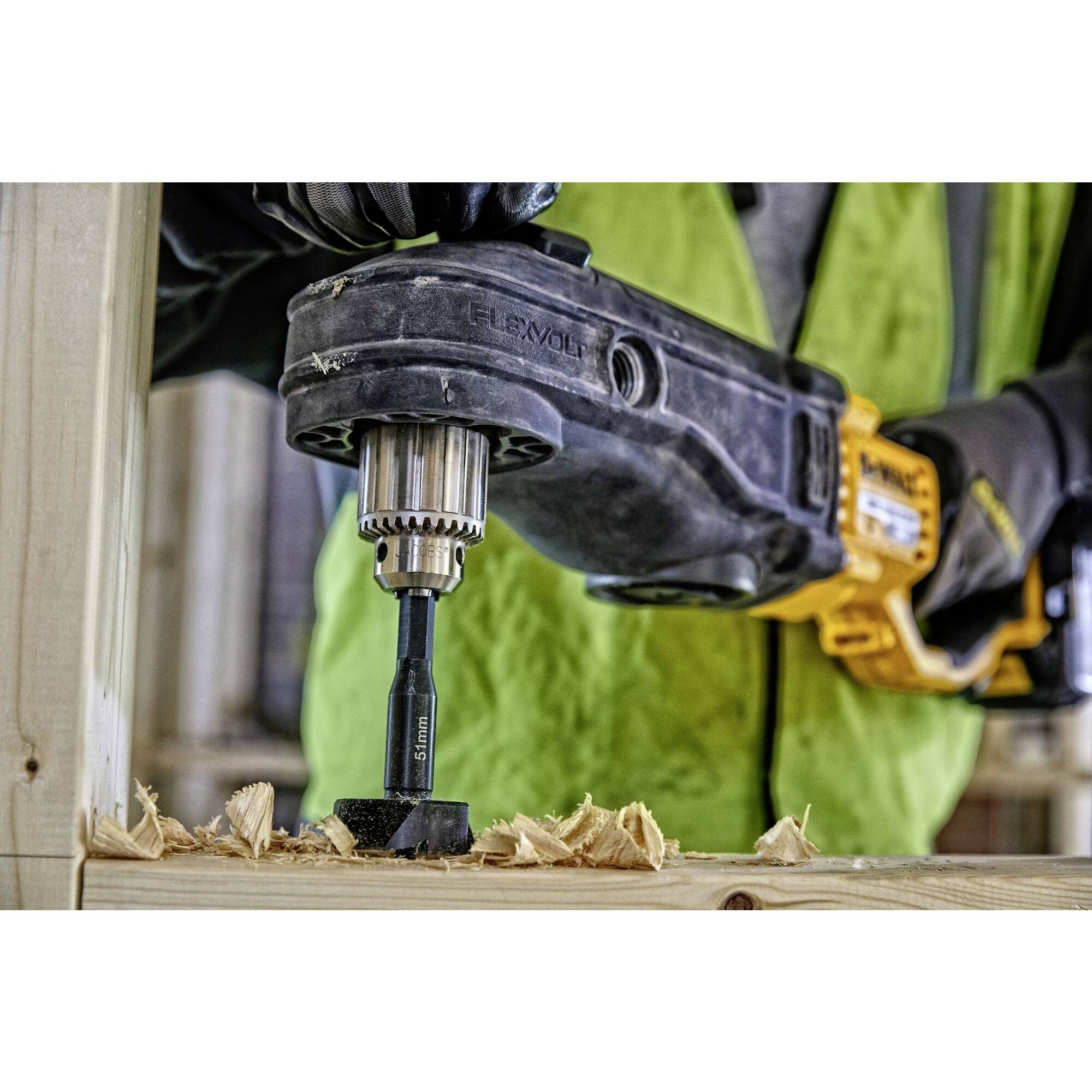 A person is using a cordless drill to bore a hole in a wooden frame. Wood shavings are scattered across the surface.