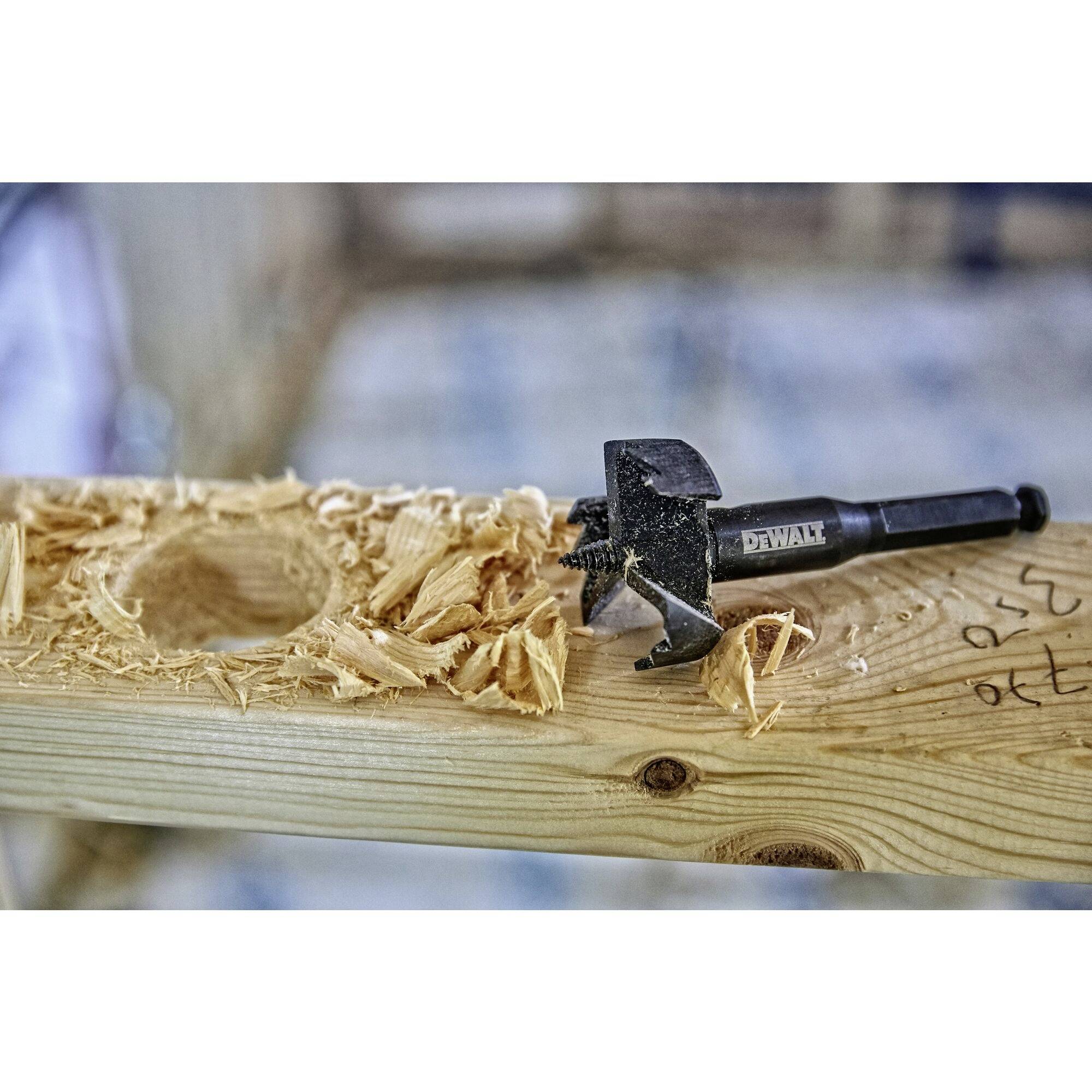A piece of wood with a hole and wood shavings beside it. A hammer is lying on top.