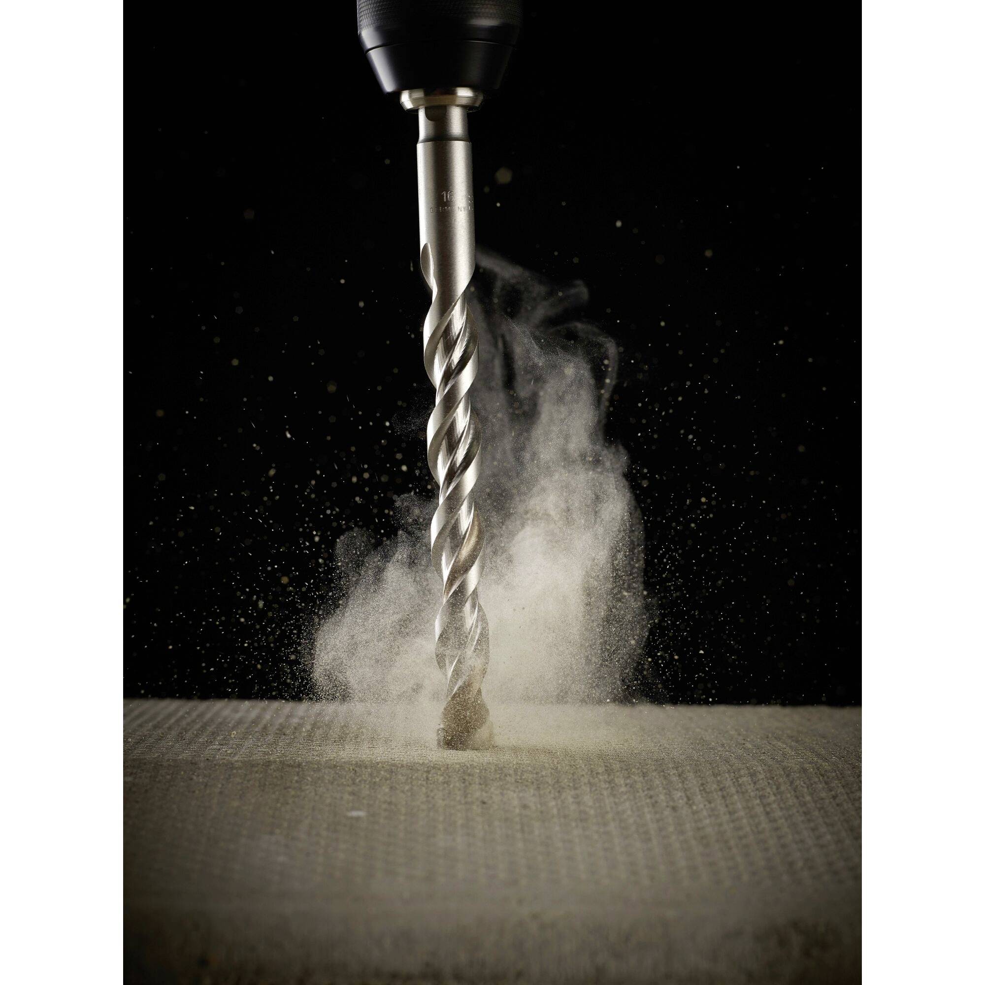 Close-up of a drill bit drilling into a concrete slab, surrounded by dust clouds. Dynamic representation of tool usage.