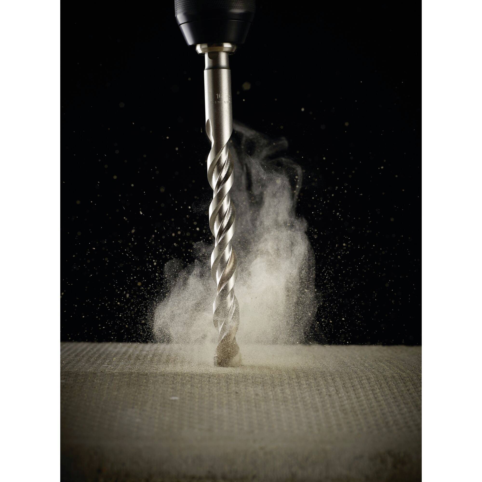 A drill bores into a material, generating swirling dust. The focus is on the movement and the resulting dust.