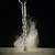 A drill penetrates material, creating dust clouds against a black background.