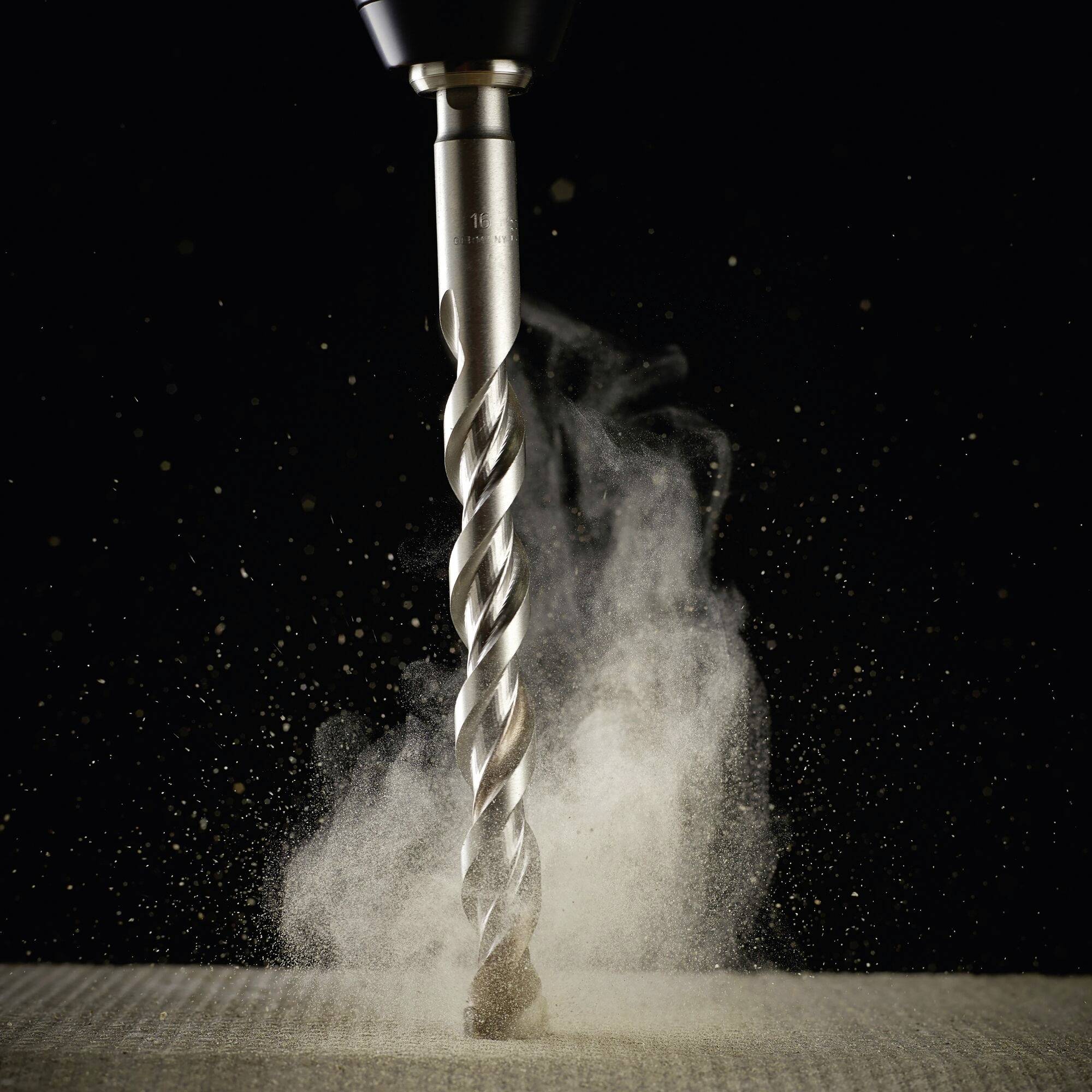 Close-up of a drill bit boring through a wooden board. Dust swirls around the drilling point.