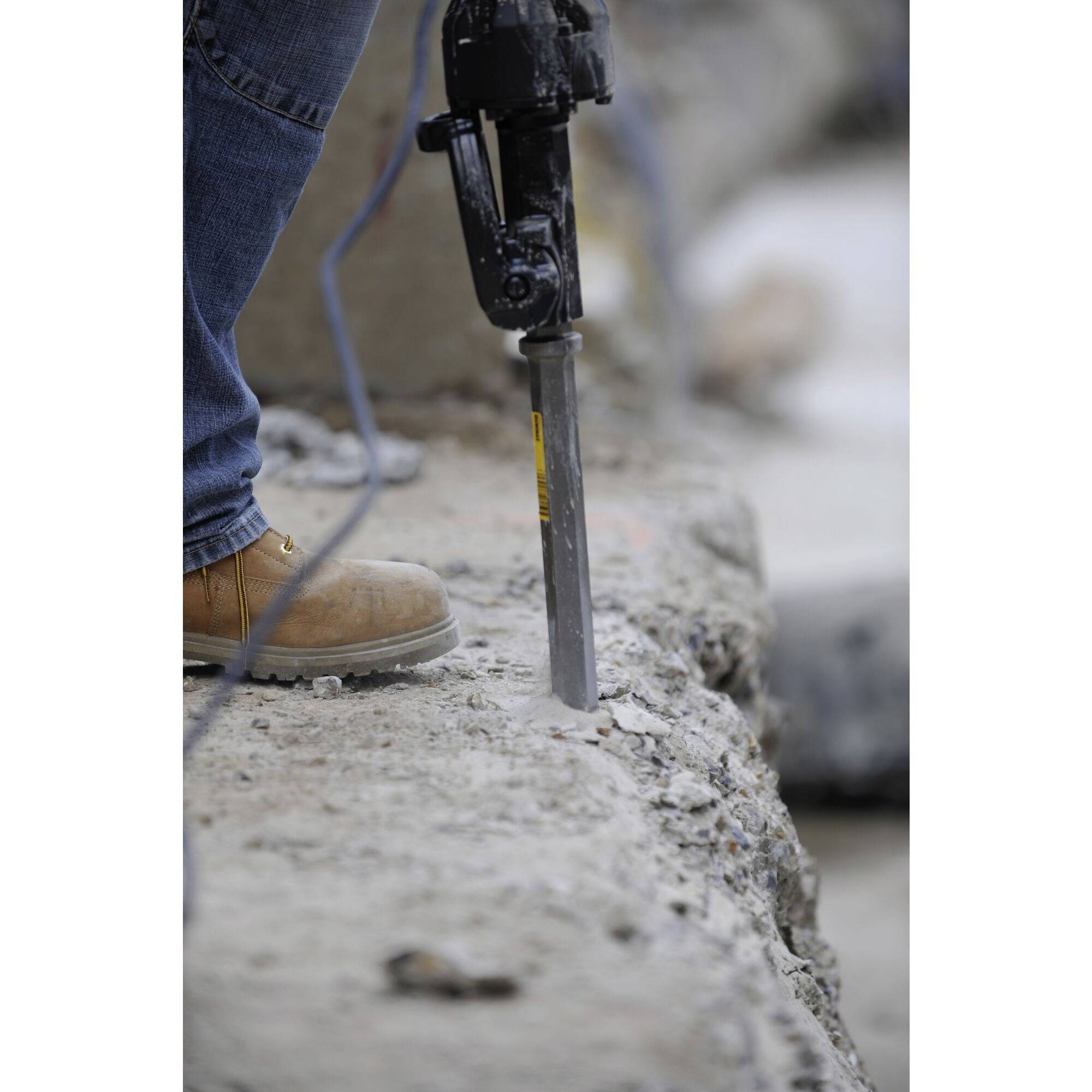 A person is using a pneumatic hammer to remove hard concrete material on a construction site. Wearing work boots.