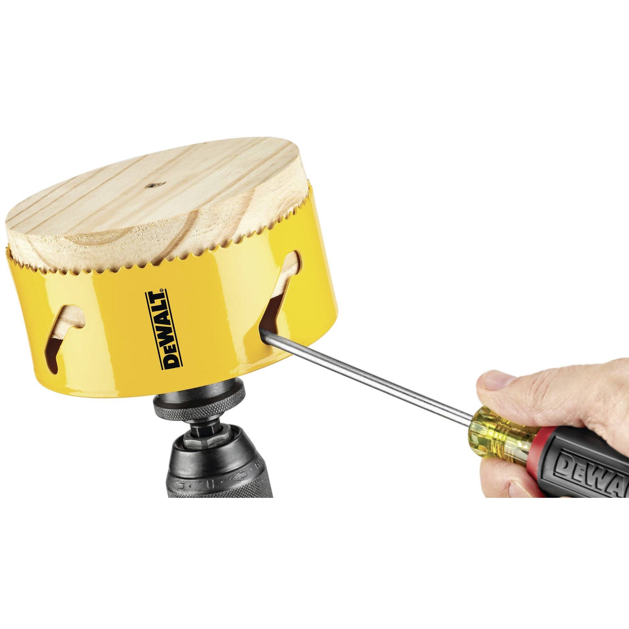 A hand holds a screwdriver and adjusts a yellow drill crown with a wooden top, which is mounted on a drill.