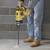 A person wearing blue jeans and work boots is using a yellow hammer drill to bore holes into a concrete wall.
