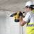 A person wearing a safety helmet and protective goggles is drilling into a concrete wall with a yellow drill.
