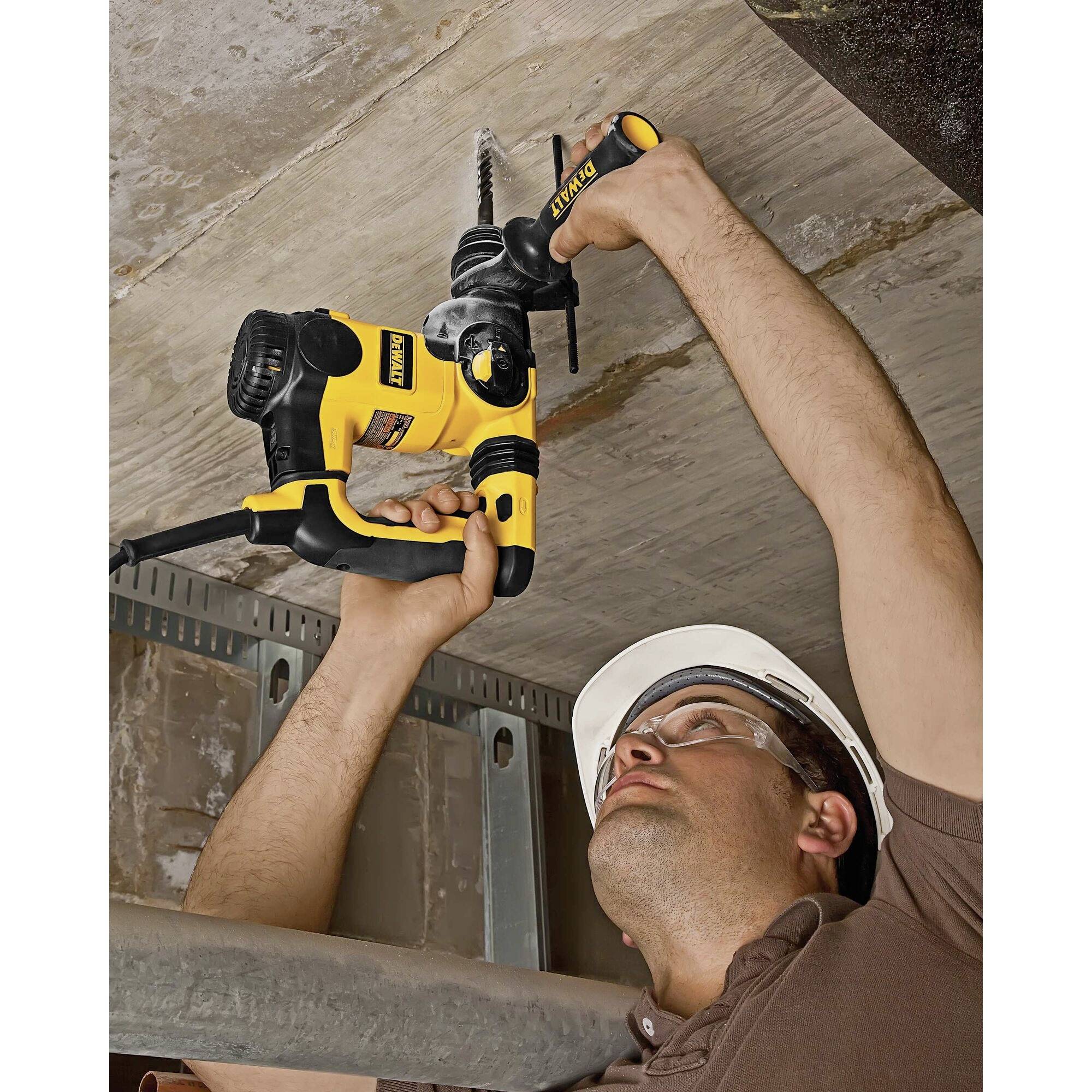 A person wearing a safety helmet is drilling into a concrete ceiling with an electric hammer drill.
