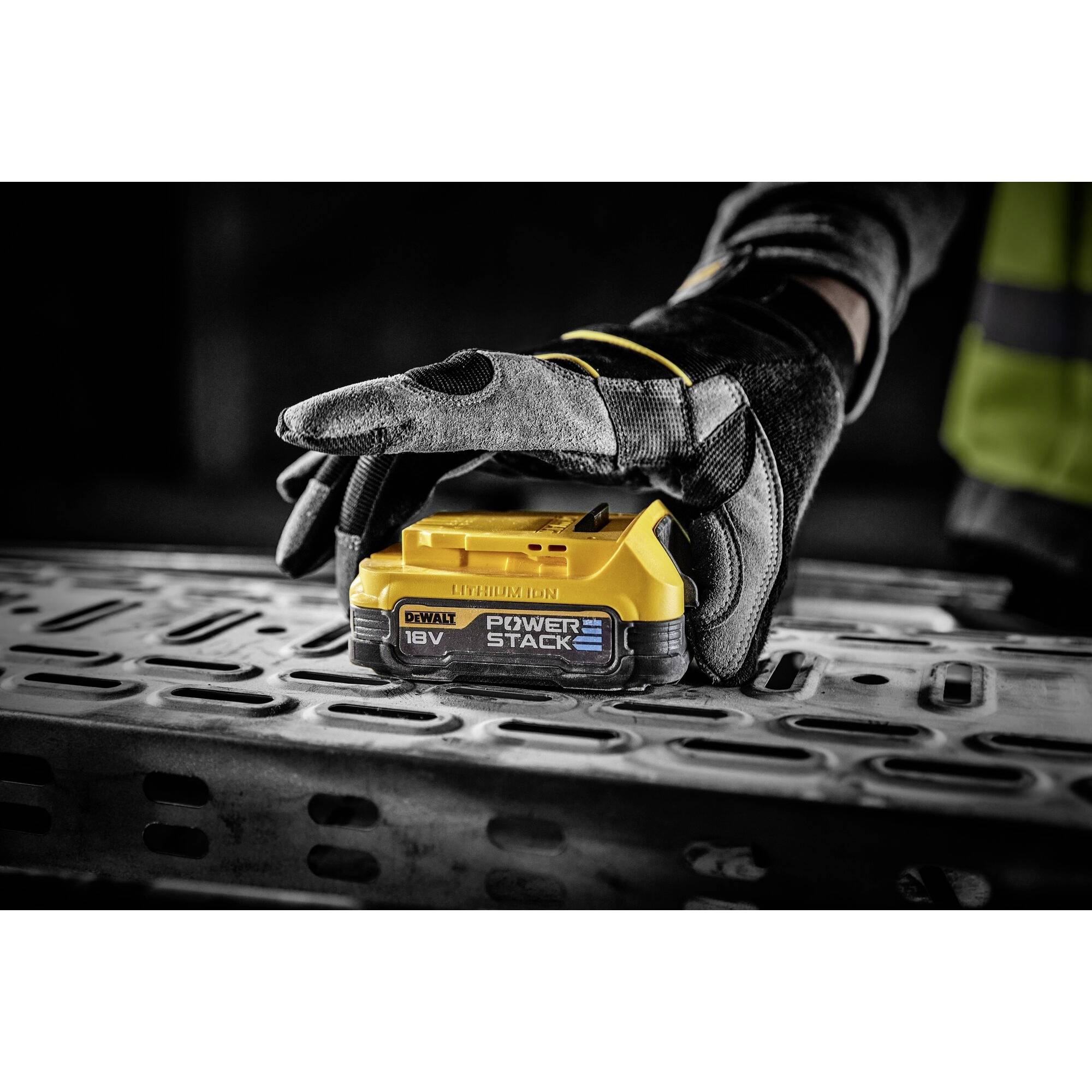 A person wearing gloves is holding a yellow battery marked as 'POWERSTACK 18V' on a metal surface.