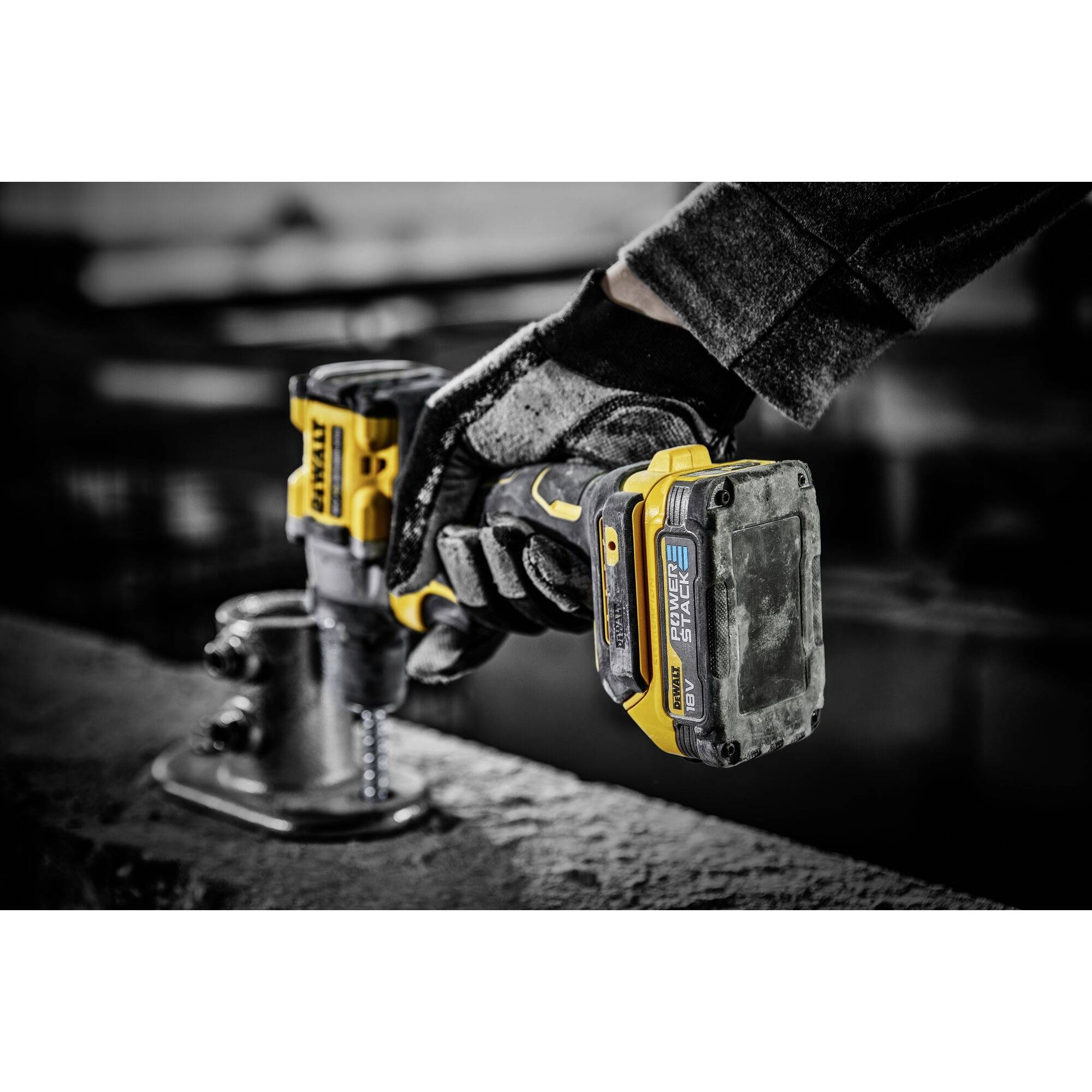 A cordless drill is being used by a person wearing gloves to drive a screw into a concrete block.