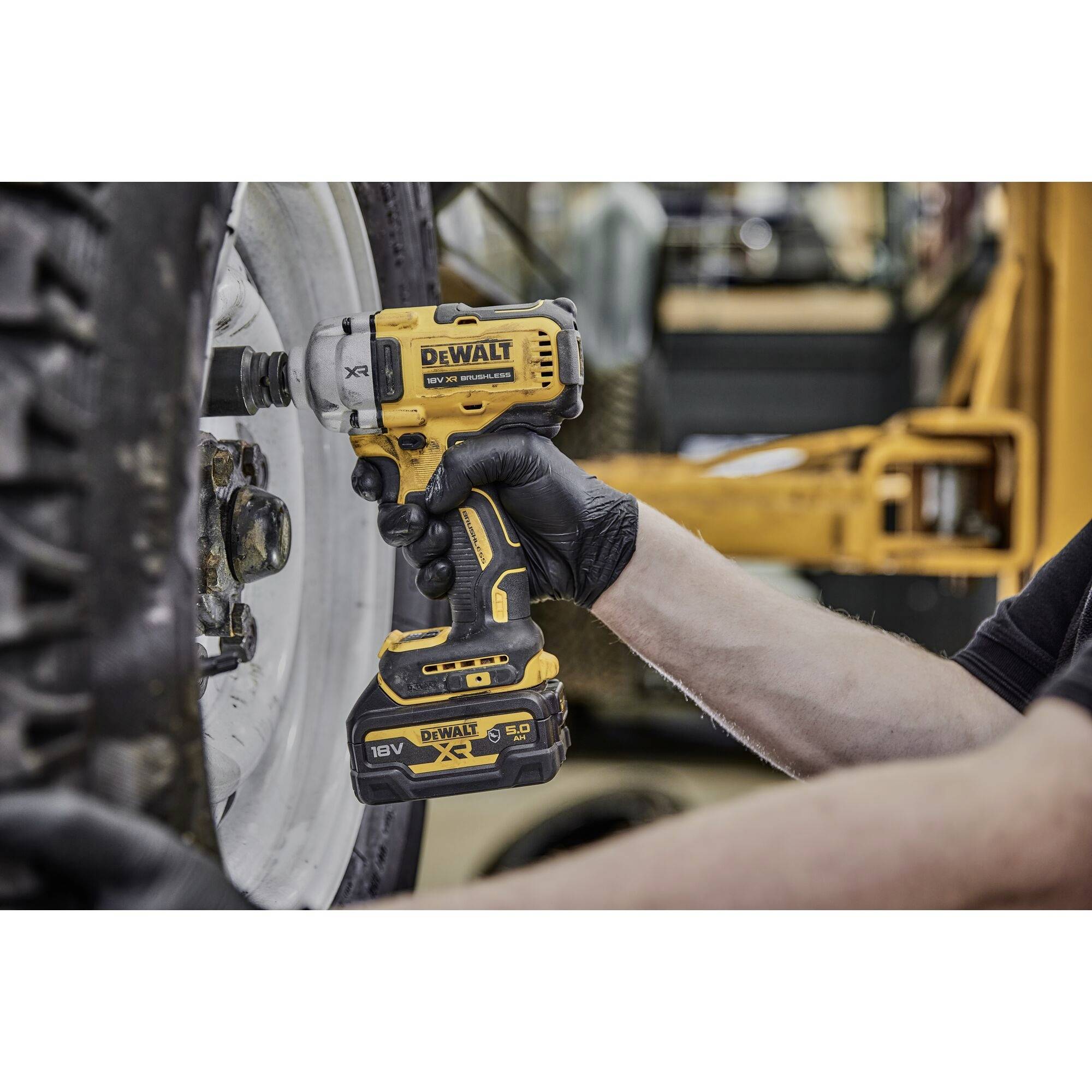 A person is using a yellow cordless drill from DeWalt to tighten a screw on a large tyre.