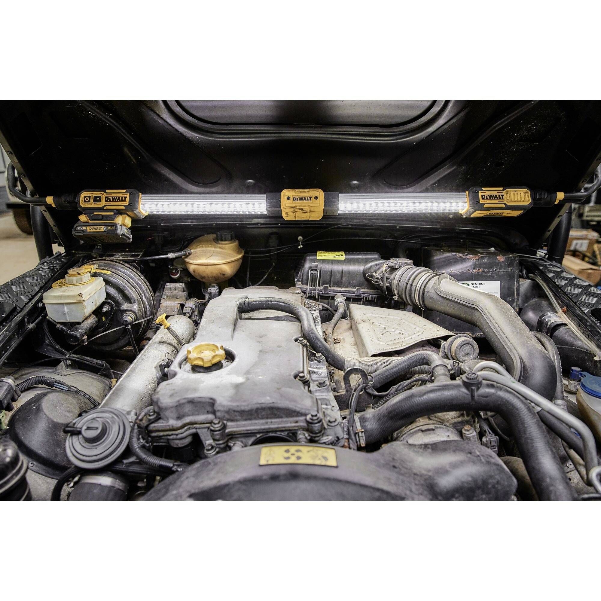 An open car engine bay showing components such as hoses, containers, and connections, illuminated by multiple lamps.