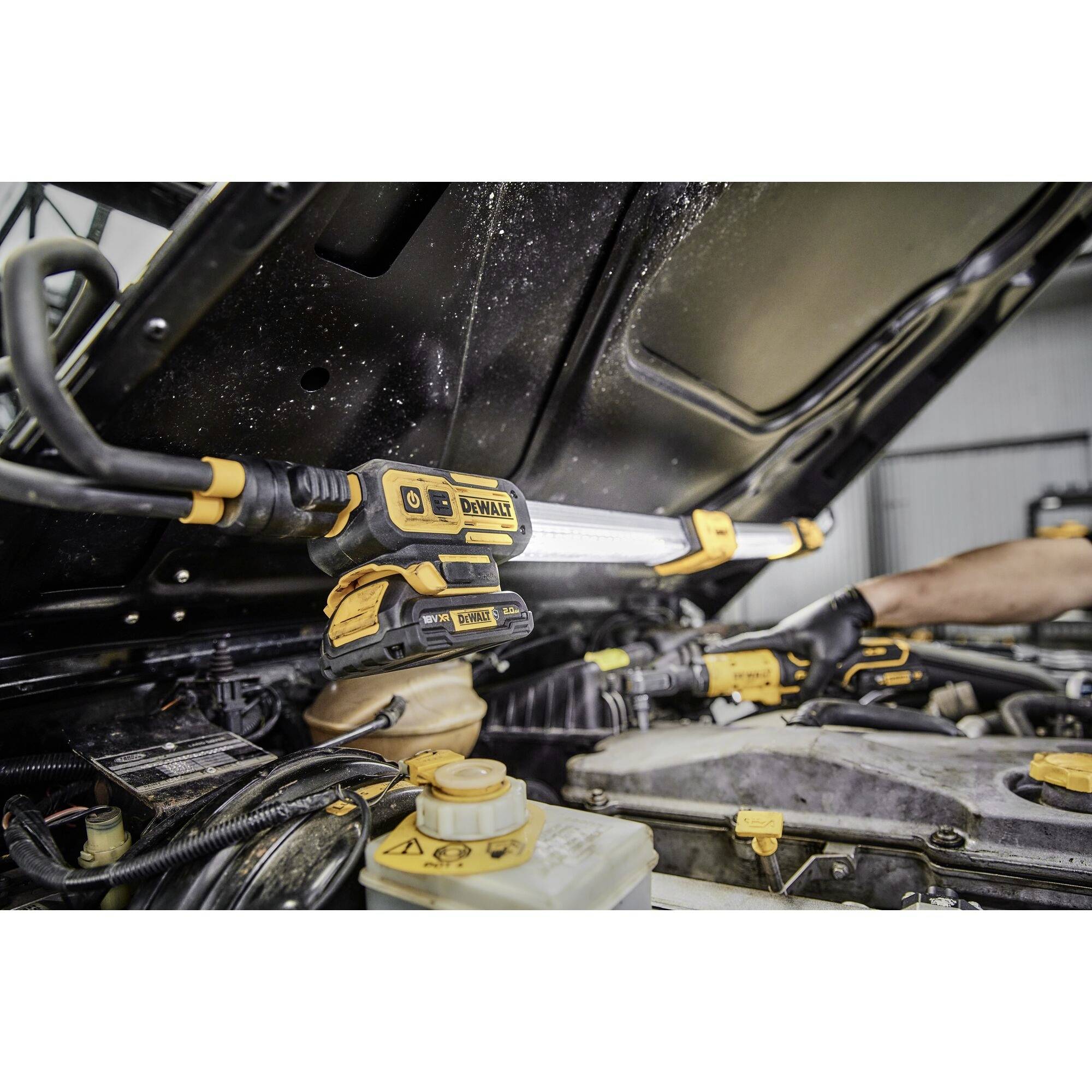 A mechanic is repairing the engine compartment of a vehicle, wearing gloves and using a torch, surrounded by various vehicle parts and tools.
