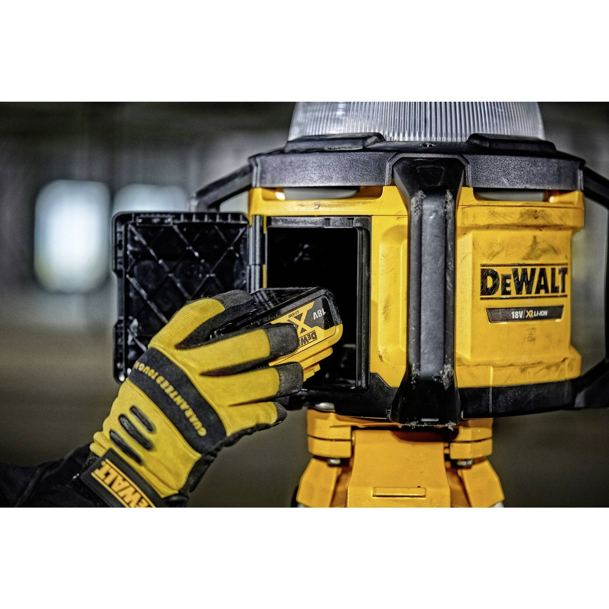 A glove holds a DeWalt battery and inserts it into a matching charger. The charger is located in a workshop environment.