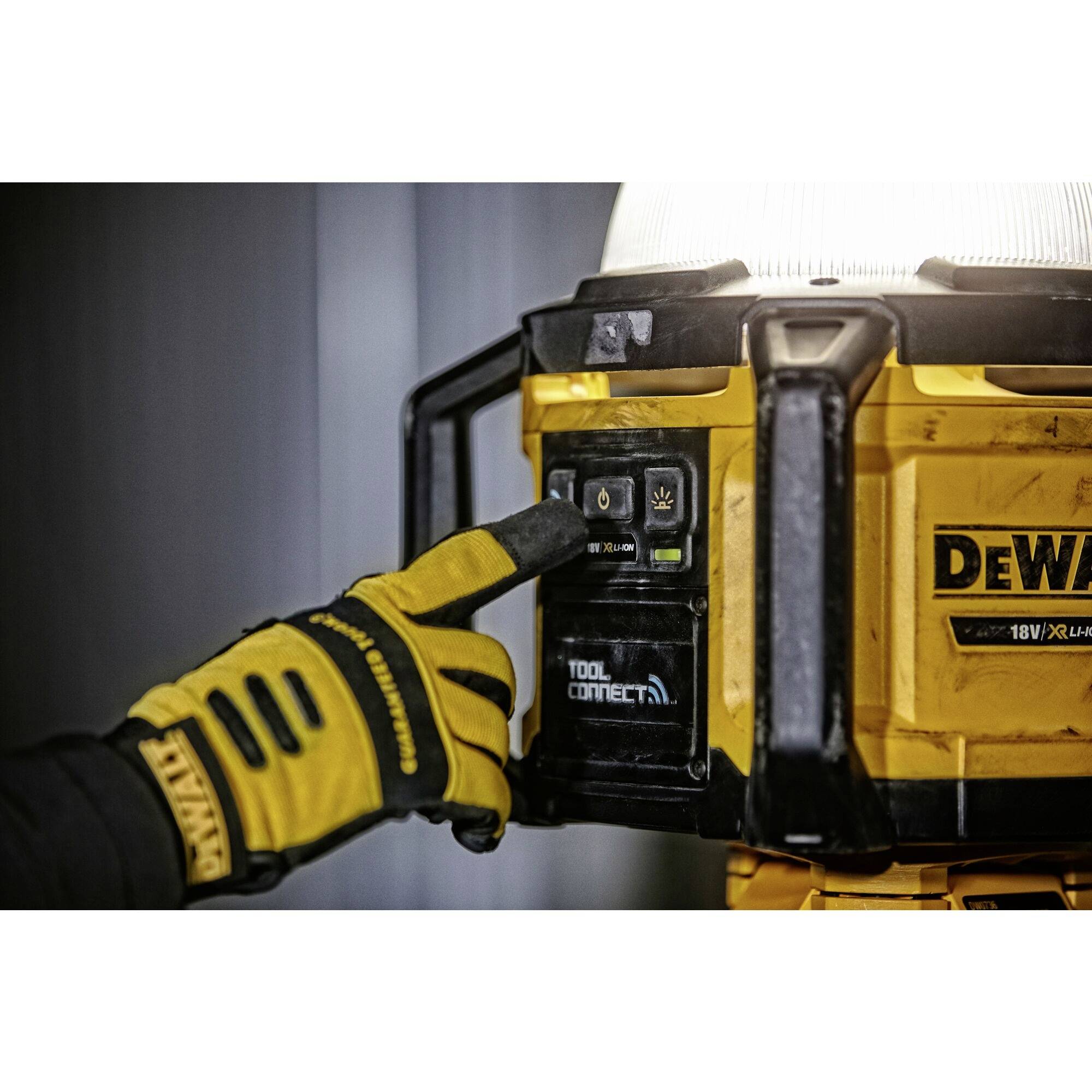 A person wearing gloves is pressing a button on a yellow, portable DeWalt construction light.