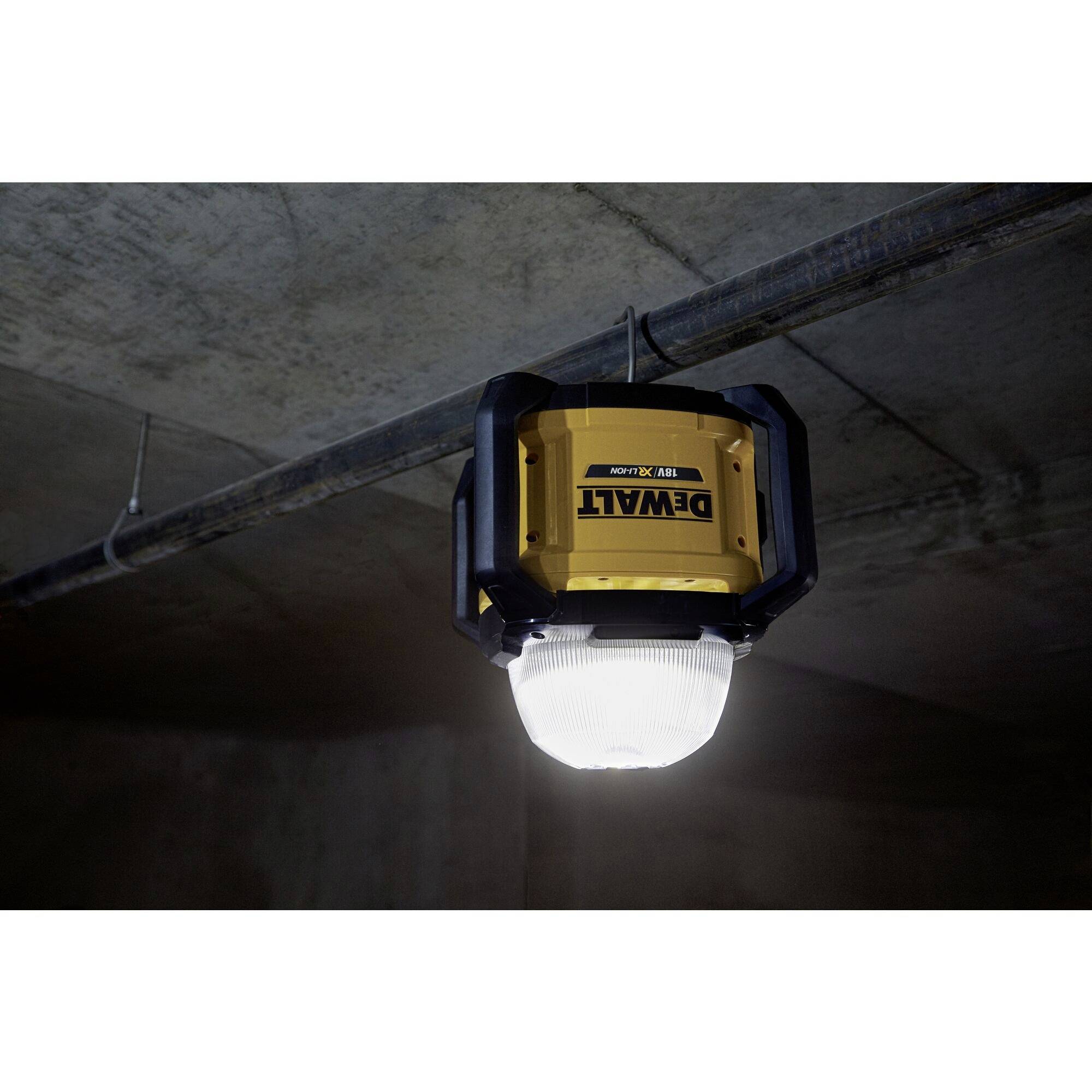 A DeWalt construction site light hanging from the ceiling, illuminating a dark concrete basement.